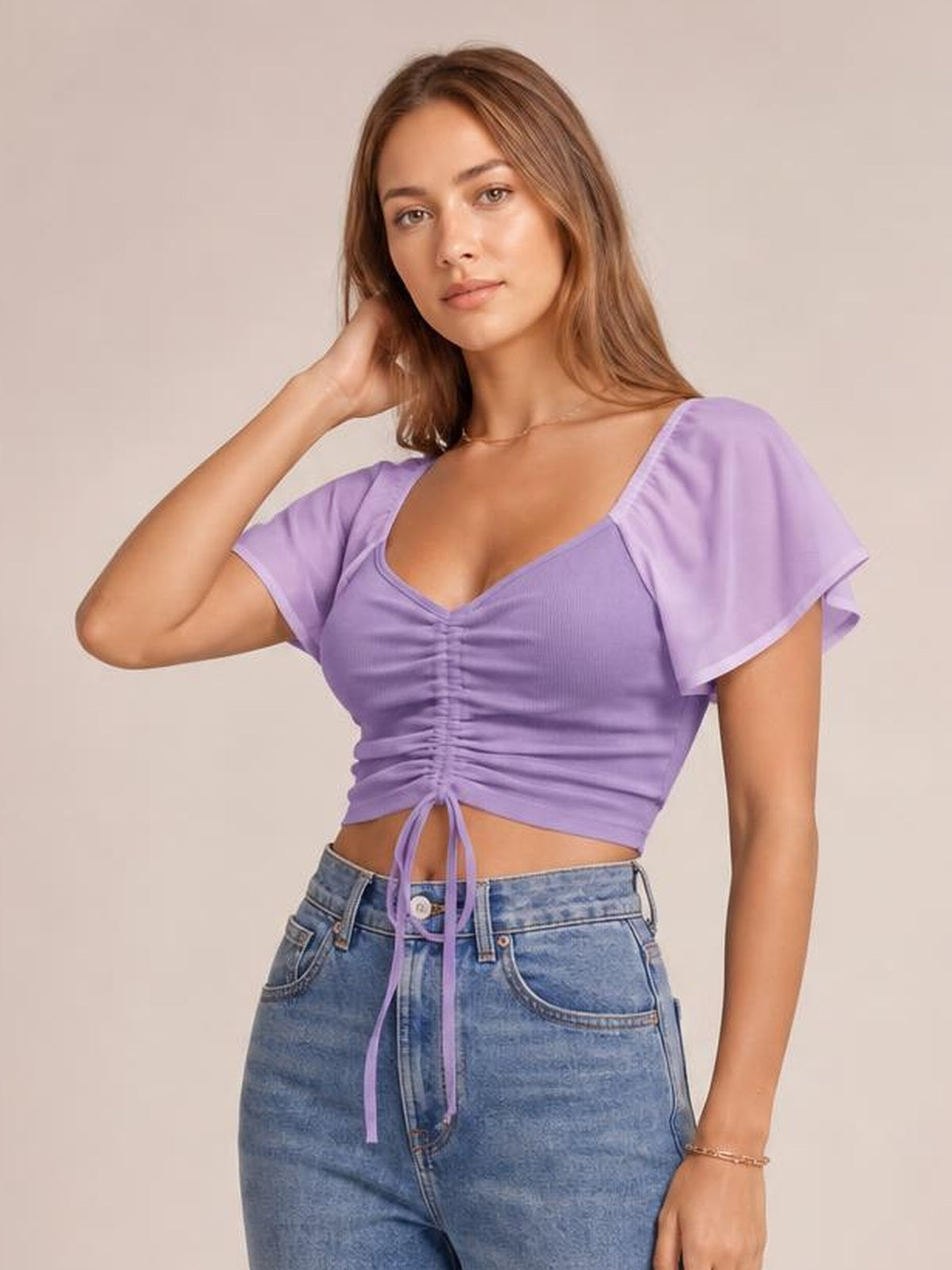 Model poses in a lilac short-sleeve crop top with a ruched drawstring front, V-neckline, and fitted silhouette.