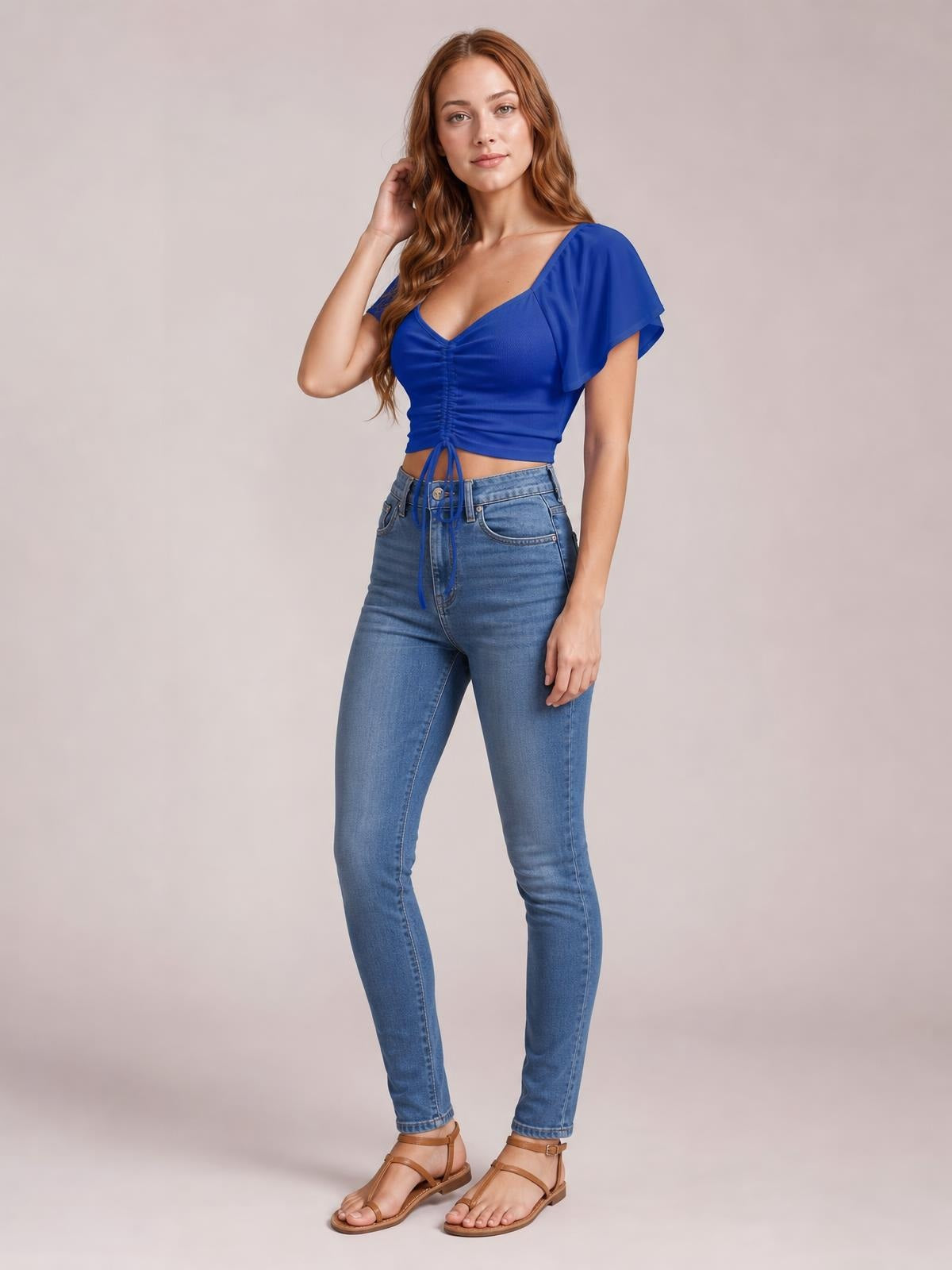 Model poses in a royal blue drawstring short sleeve crop top with a ruched front, flutter sleeves, V-neckline, and fitted silhouette.