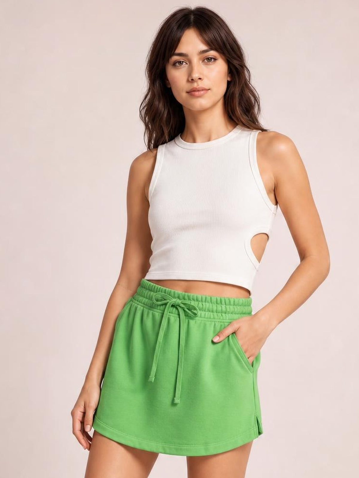 A model poses with one hand in the pocket of a bright green solid mini skort featuring a drawstring elastic waistband and skirt-like silhouette.