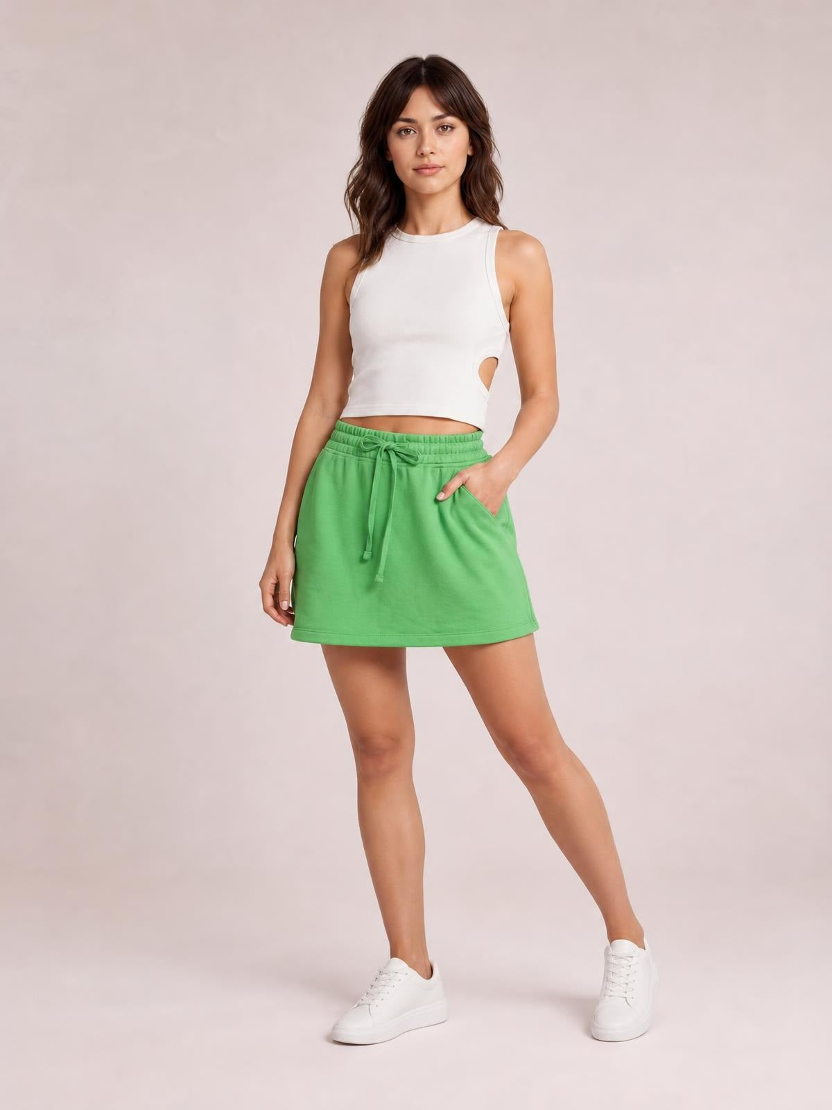 Model poses in a bright green solid mini skort with a drawstring waistband, skirt-like silhouette, visible side pocket, and relaxed fit.