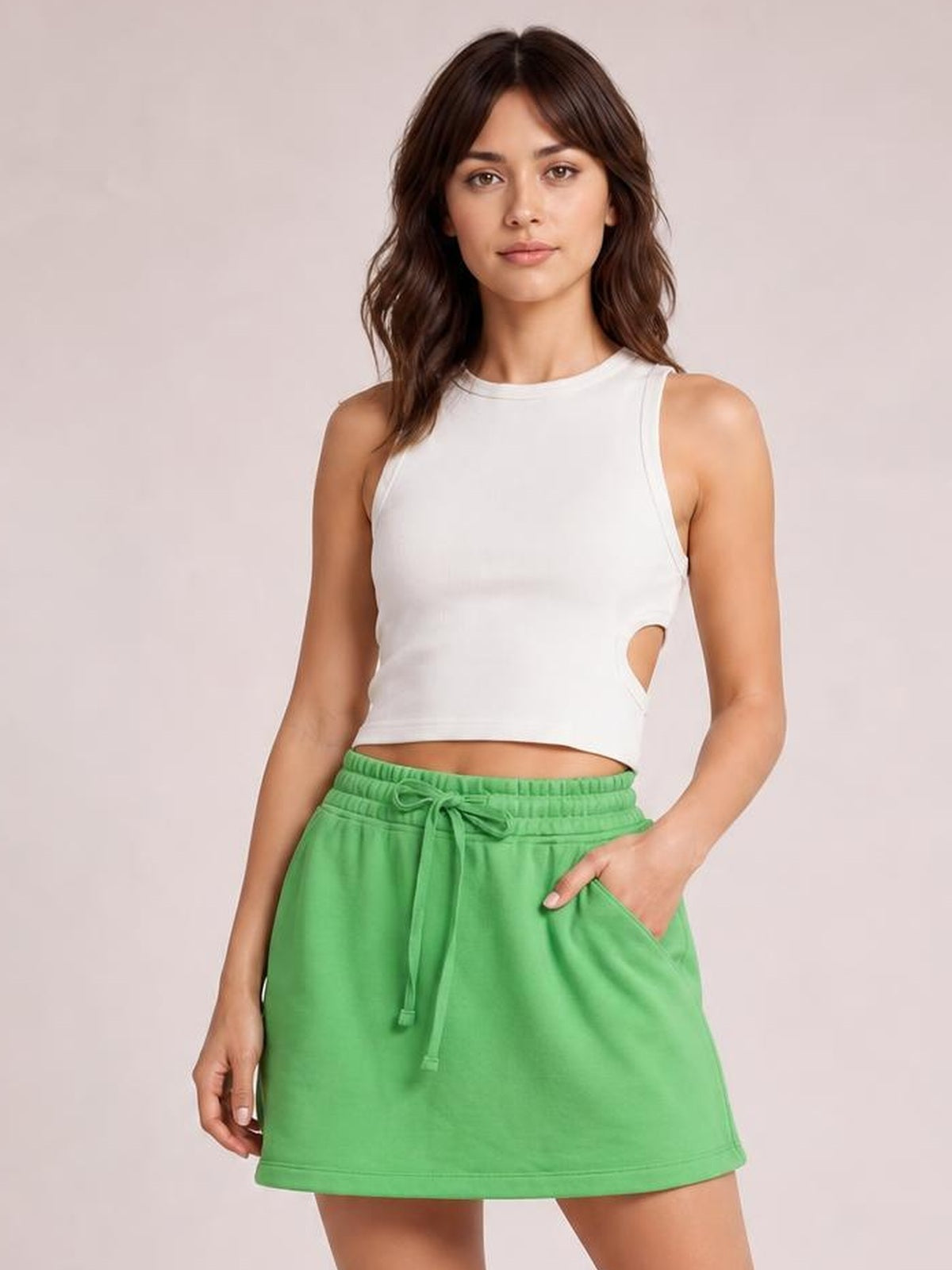Model poses in a bright green solid mini skort with a drawstring waistband and skirt-like silhouette, slipping one hand into the side pocket.
