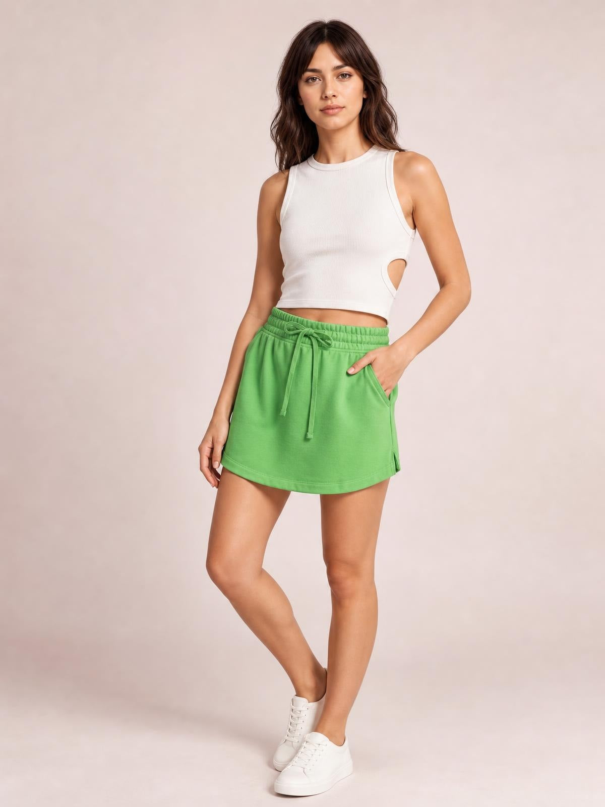 Model poses in a bright green solid mini skort with a drawstring waist, elastic waistband, curved hem, and relaxed skirt-like silhouette.