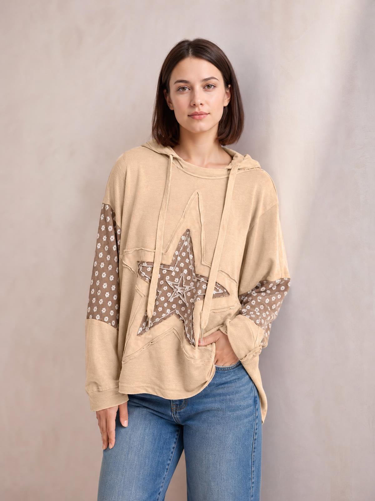 Model wears a relaxed beige drawstring star hoodie with long sleeves, floral-patterned contrast panels, raw-edge seams, and an oversized silhouette.