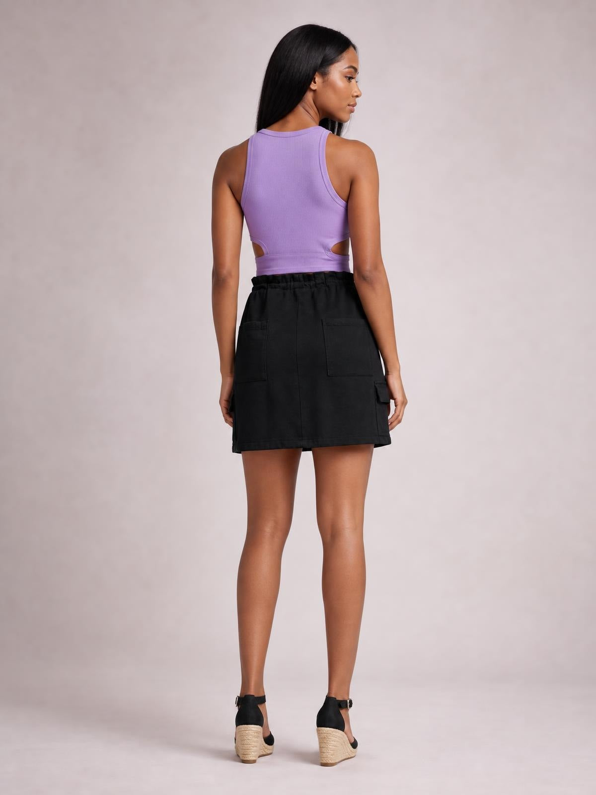 Model shown from behind wearing a black denim mini skirt with a drawstring waist, straight hem, relaxed silhouette, and two large back patch pockets.