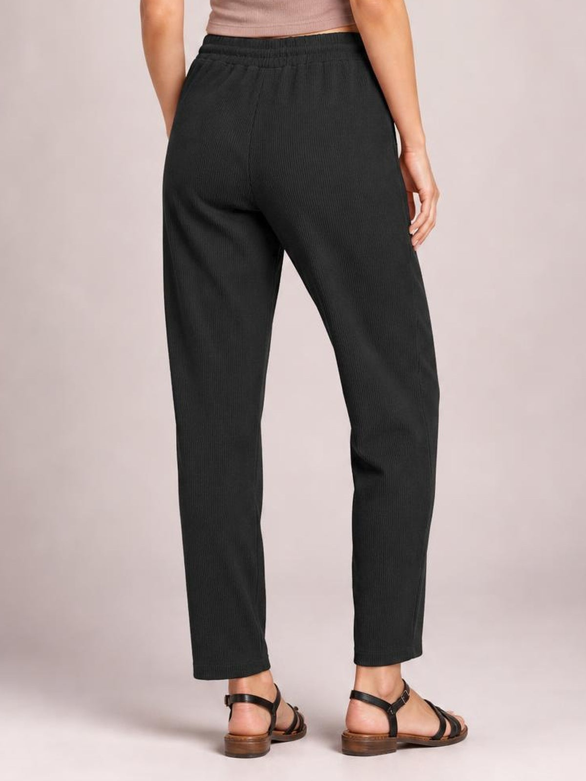 Model poses from the back in black drawstring straight pants with an elastic waist, side pockets, subtle texture, and a relaxed straight-leg silhouette.