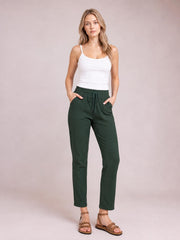 Model wearing dark green drawstring straight pants with a relaxed silhouette, visible side pockets, and cropped hems, posing with hands in the pockets.