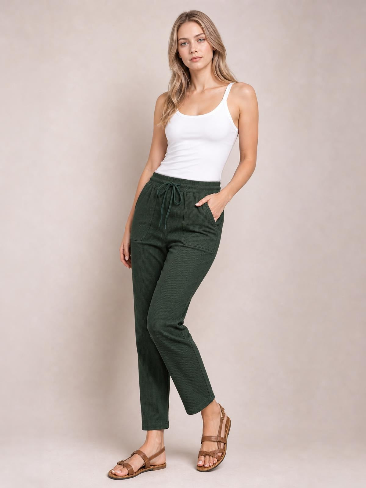 Model poses in dark green drawstring straight pants with an elastic waist, visible pockets, and a relaxed ankle-length silhouette.