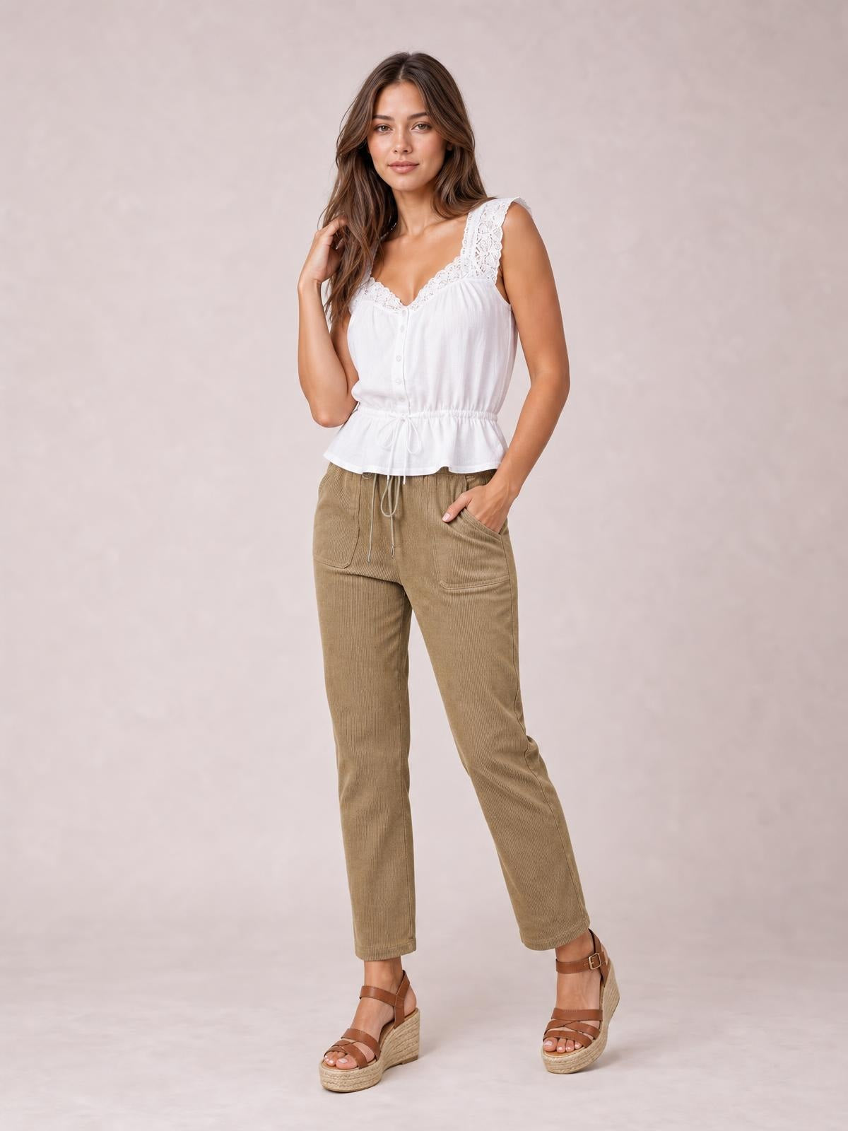 A model poses in tan drawstring straight-leg pants with visible front pockets, an easy silhouette, and one hand tucked into a pocket.