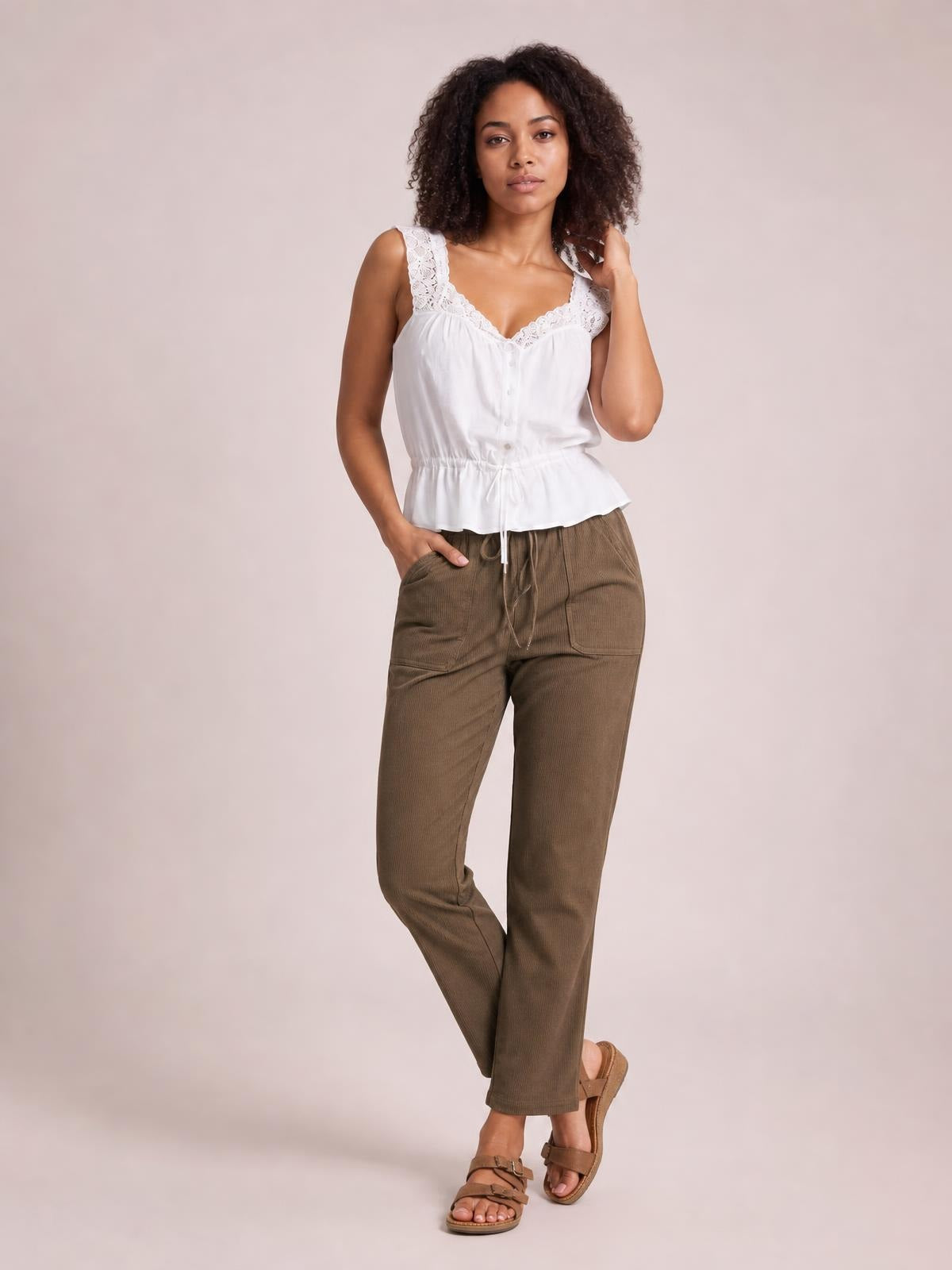 A model poses in brown drawstring straight pants with visible side pockets, a relaxed straight-leg silhouette, and one hand tucked into a pocket.