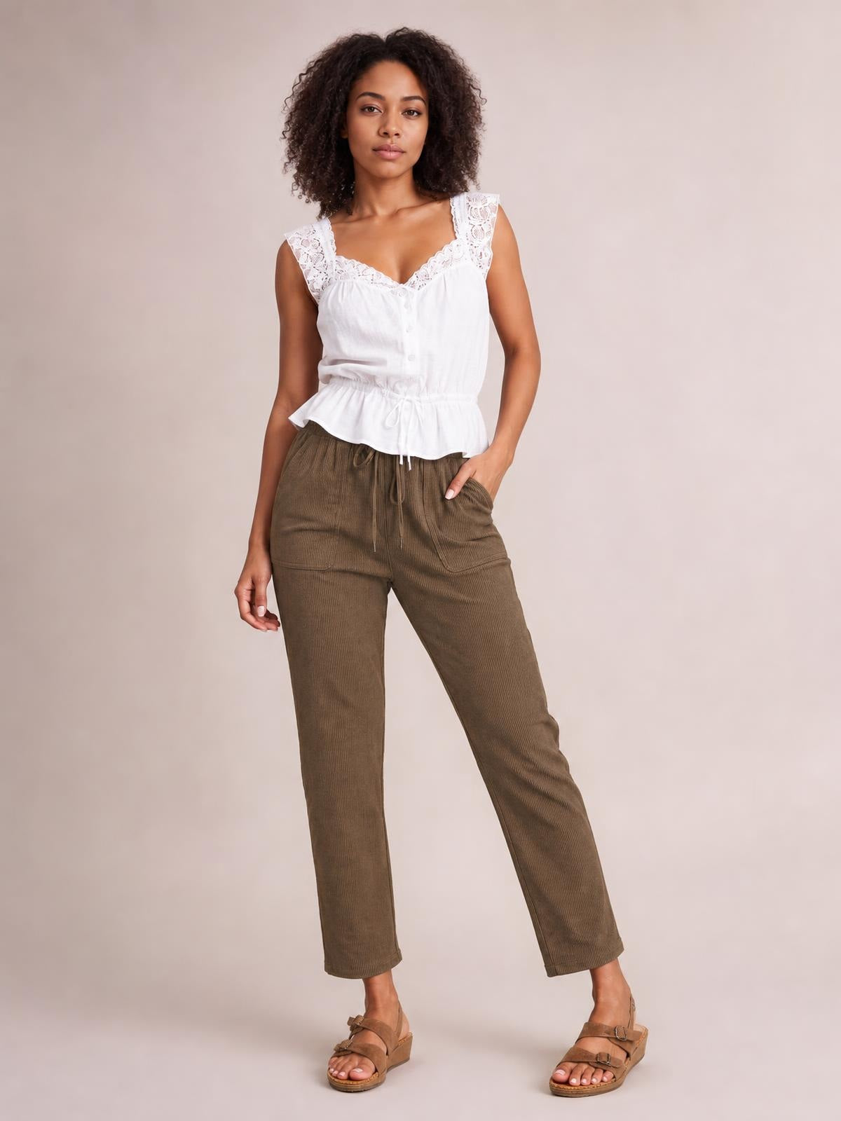 Model wears brown drawstring straight pants with a relaxed straight-leg silhouette, visible pockets, and one hand tucked into a pocket.