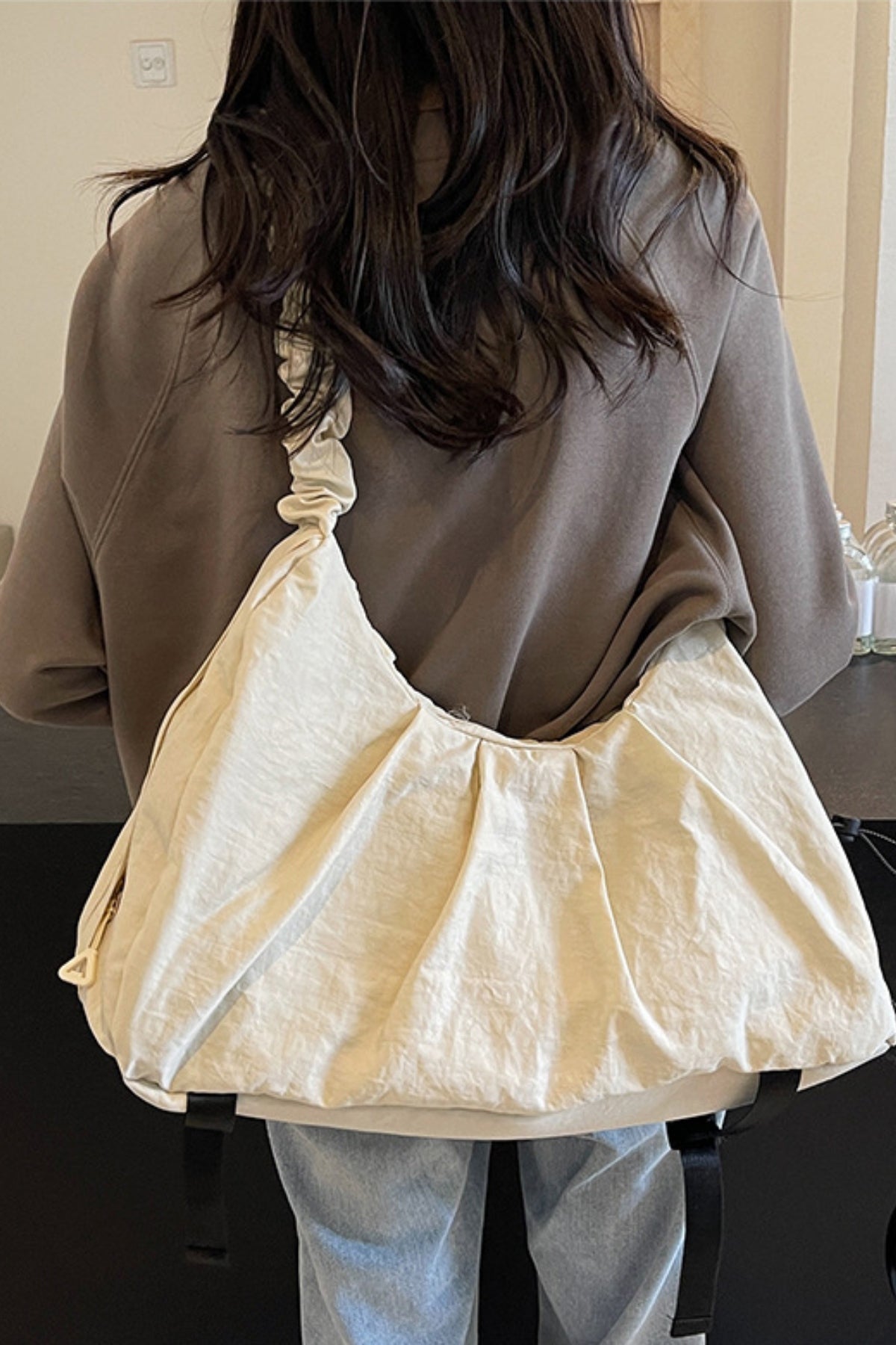 Model wearing a large cream ruched crossbody bag with a gathered drawstring strap, softly structured slouchy silhouette, and lightweight cloth construction.