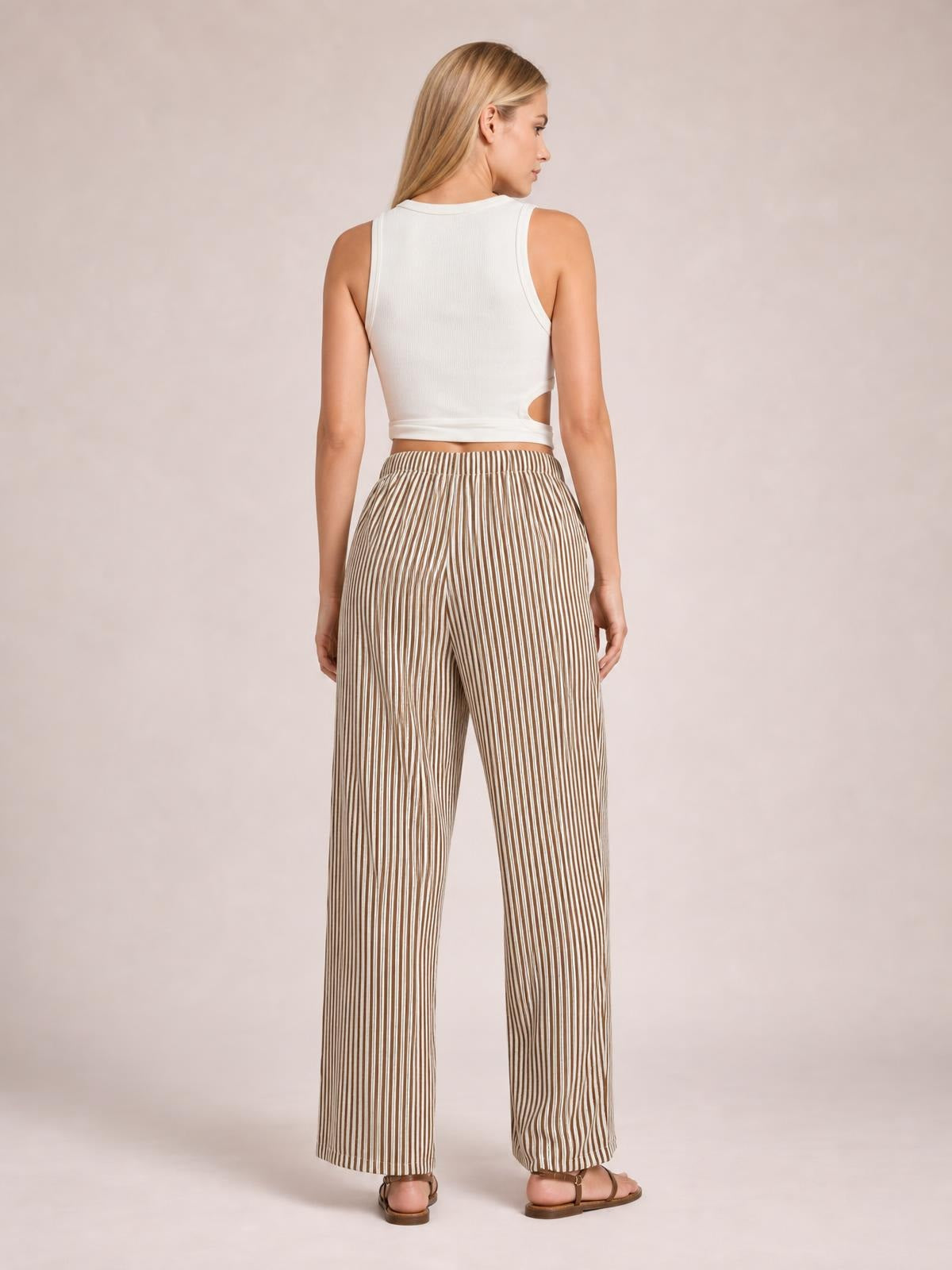 A model stands facing away in brown-and-cream vertically striped pants with an elastic waist and relaxed wide-leg silhouette.