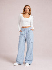 Model poses with hands in the pockets of light blue striped wide-leg cargo pants featuring a drawstring waist and utility patch pockets.
