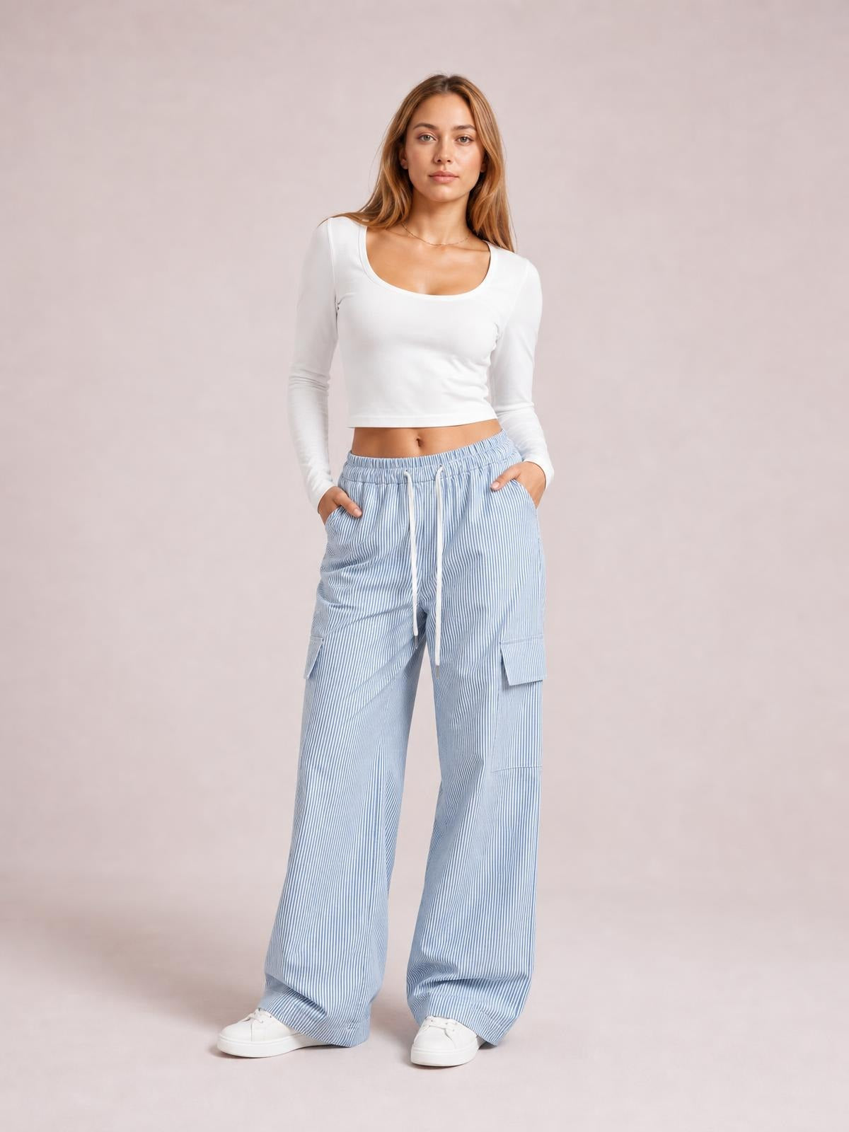 Model poses with hands in the pockets of light blue striped wide-leg cargo pants featuring a drawstring waist and utility patch pockets.