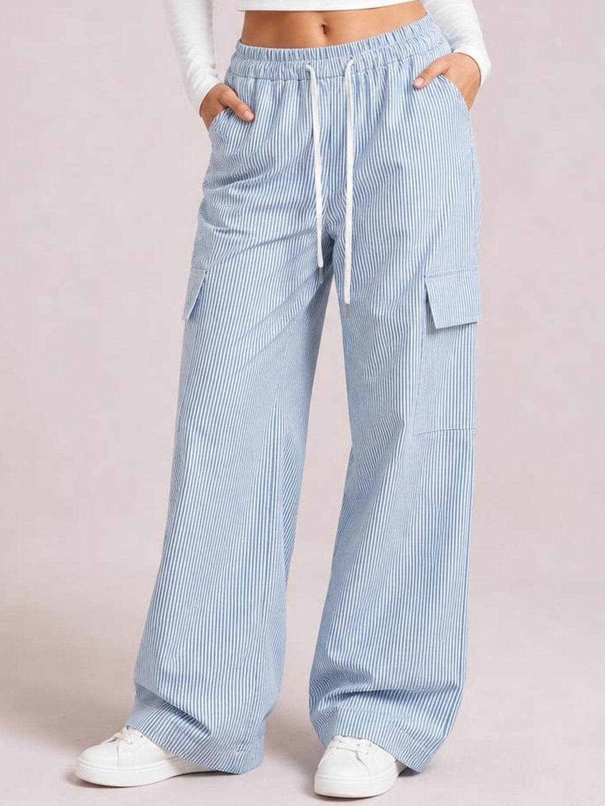 Model stands with hands in the pockets, wearing light blue striped wide-leg cargo pants with a drawstring waist and flap cargo pockets.