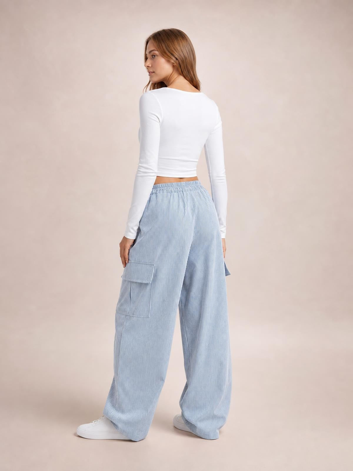 Model turned slightly away wears light blue striped drawstring cargo pants with a wide-leg silhouette, elastic waistband, and large side pockets.