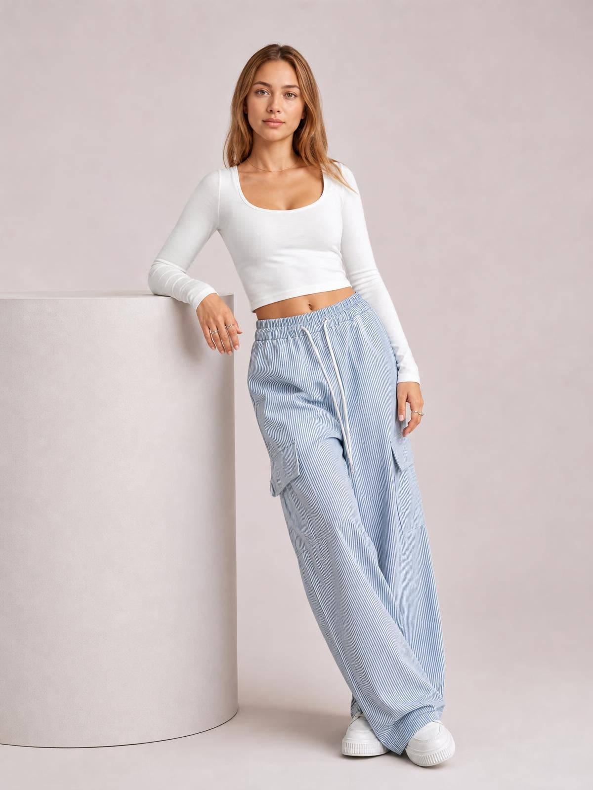 Model poses in light blue and white striped wide-leg cargo pants with a drawstring waist, side pockets, and relaxed flowing silhouette.