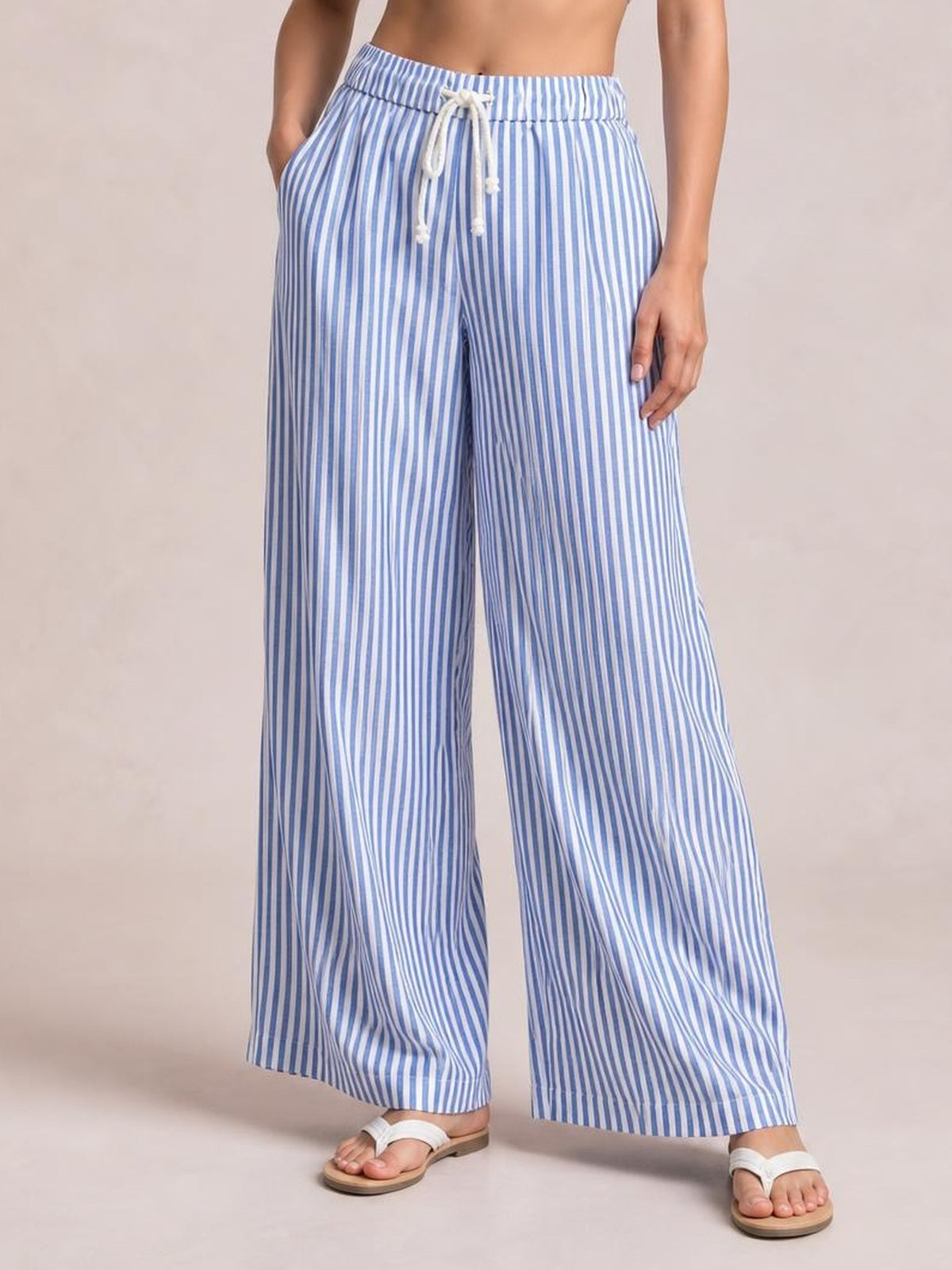 Model wears blue-and-white striped wide-leg pants with a drawstring waistband, relaxed flowing silhouette, side pockets, and hands resting in the pockets.