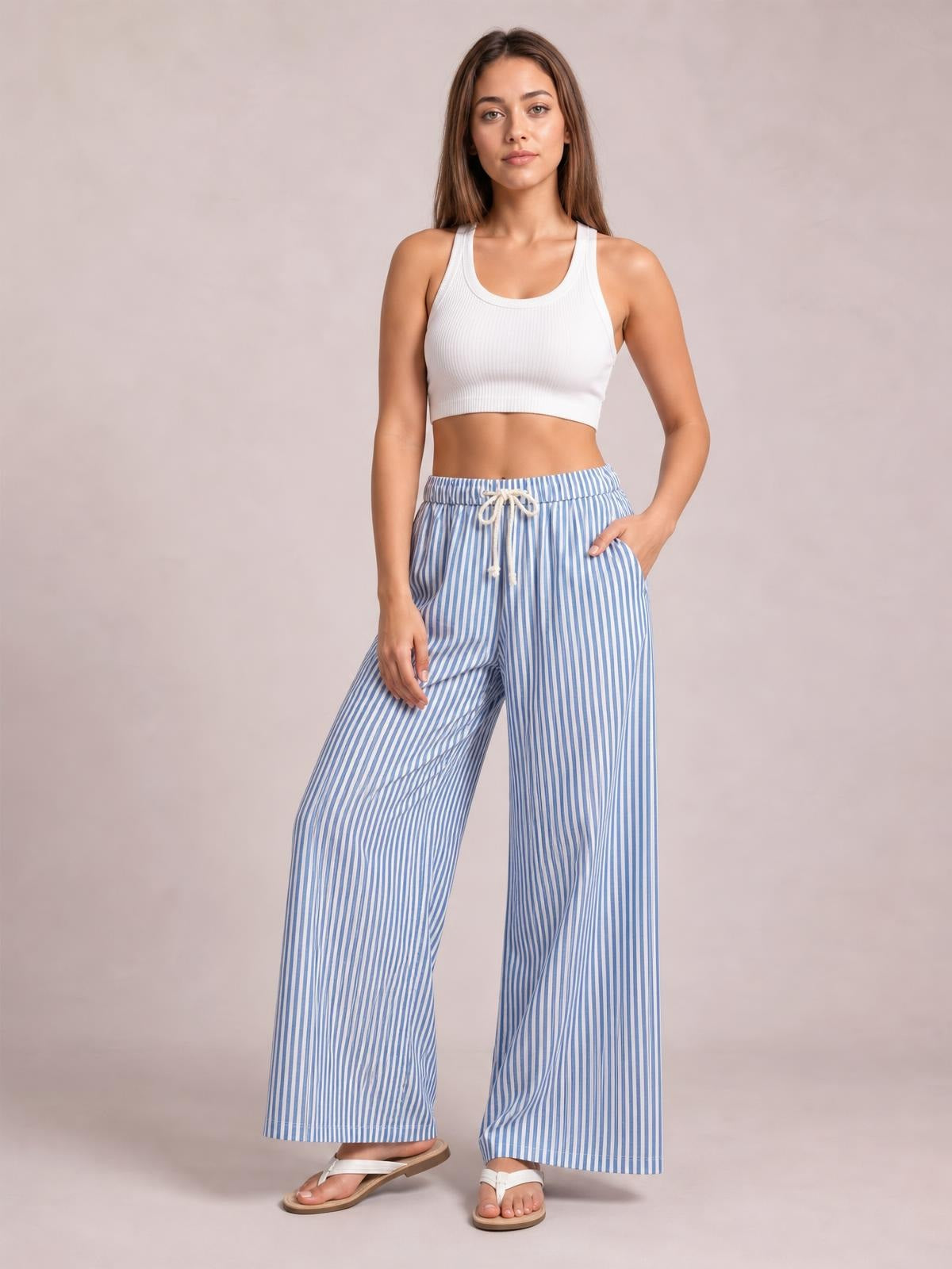 Model poses in blue-and-white striped wide-leg pants with a drawstring waist, relaxed flowing silhouette, and one hand tucked into a pocket.