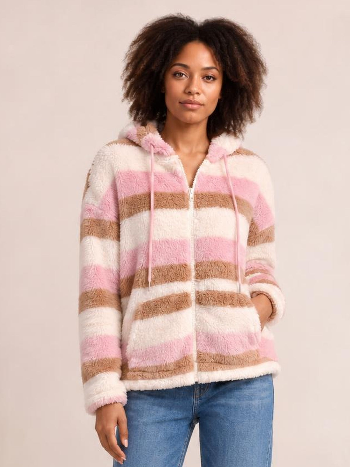 Model poses in a relaxed stance wearing a plush pink, cream, and tan striped zip-up hooded jacket with drawstrings, long sleeves, and a straight silhouette.
