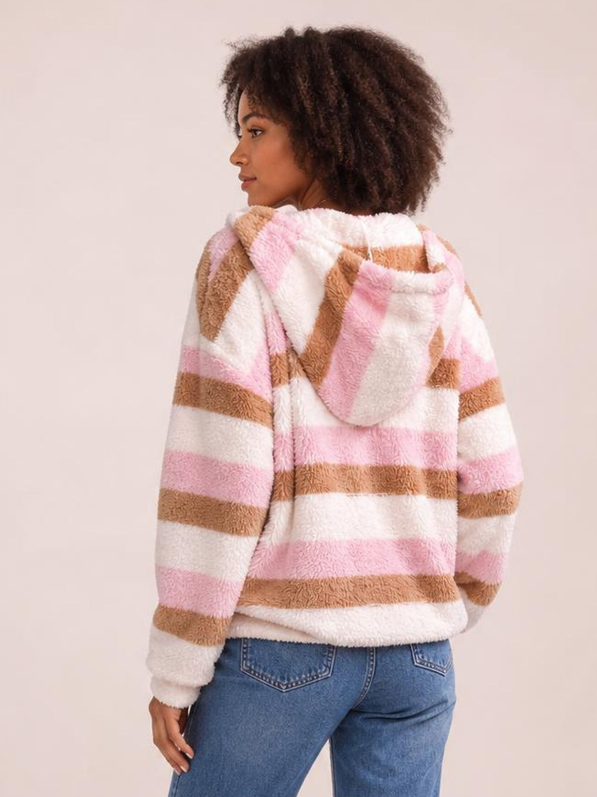 A woman looks over her shoulder wearing a relaxed striped hooded jacket in pink, white, and brown with long sleeves and a softly textured finish.