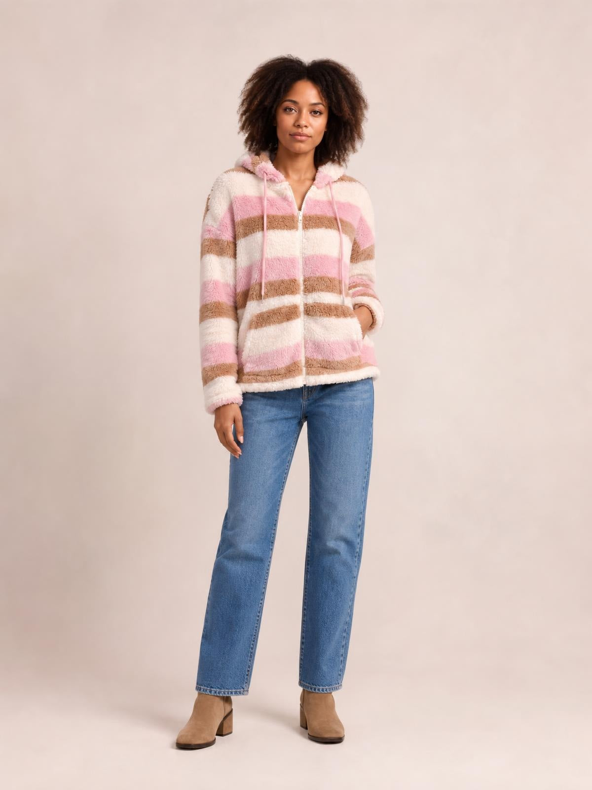 Model stands wearing a pink, cream, and brown striped zip-up hooded jacket with drawstrings, long sleeves, and a relaxed silhouette.