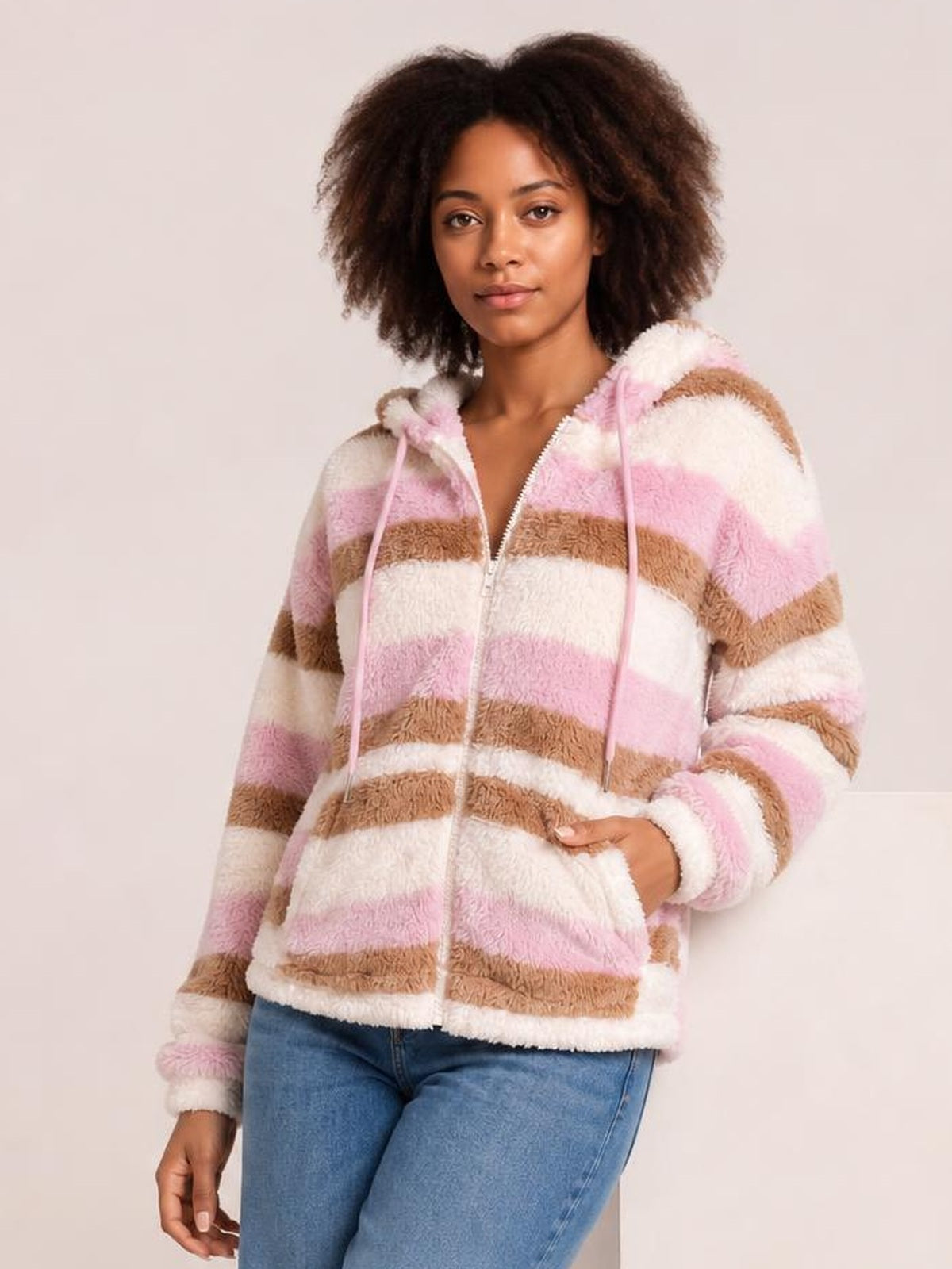 Model wears a relaxed striped zip-up hooded jacket in pink, cream, and brown, with a fuzzy texture, drawstring hood, front zipper, and long sleeves.