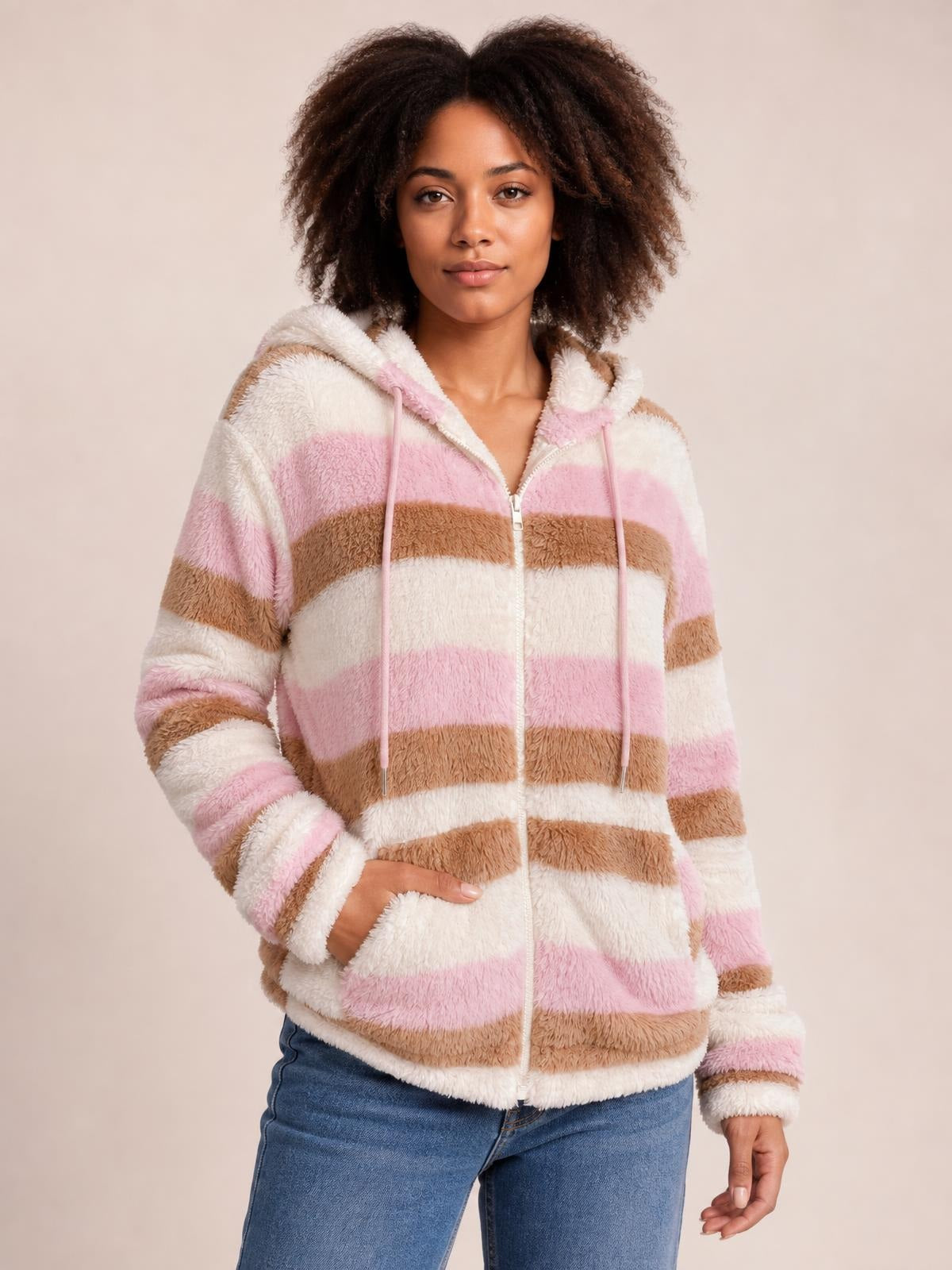 A model poses in a pink, cream, and brown striped zip-up hooded jacket with drawstrings, plush texture, long sleeves, and a relaxed silhouette.