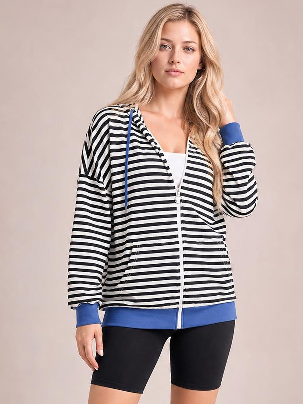 A model poses in a relaxed black-and-white striped zip-up hoodie with blue drawstrings, cuffs, hem, long sleeves, and front pockets.