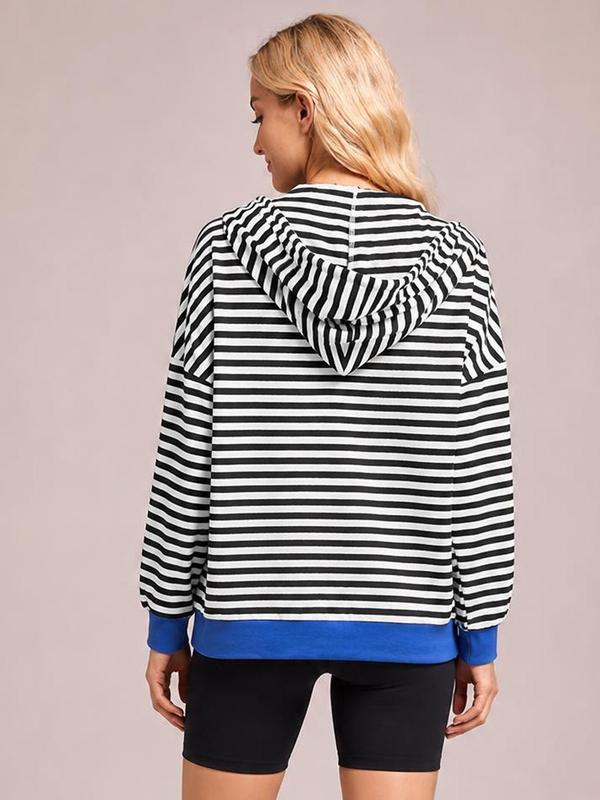 Model shown from the back wears a black-and-white striped zip-up long-sleeve hoodie with a drawstring hood, blue cuffs, and a relaxed silhouette.