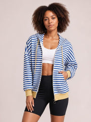Model wears a blue-and-white striped zip-up long-sleeve hoodie with drawstring hood, pockets, and a relaxed silhouette, posing with one hand tucked inside.