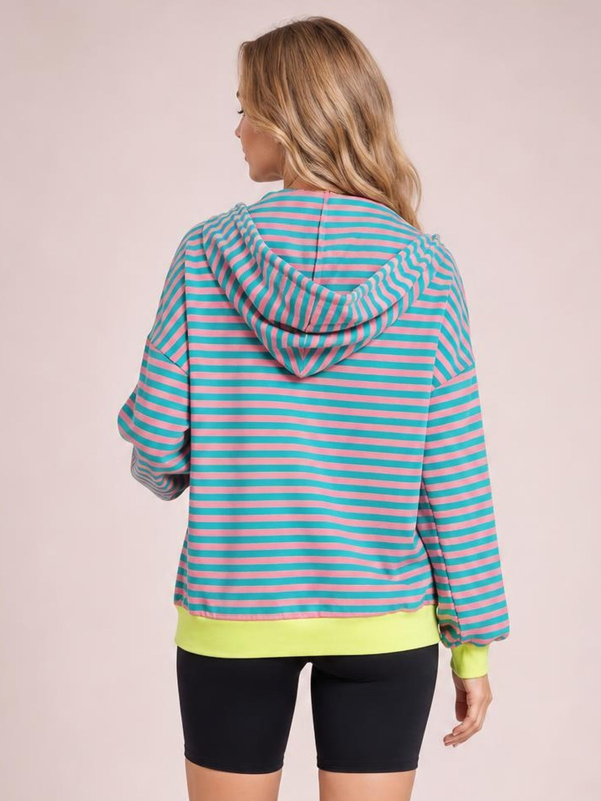 A model poses from the back in a turquoise and pink striped zip-up hoodie with a relaxed silhouette, long sleeves, and a drawstring hood.