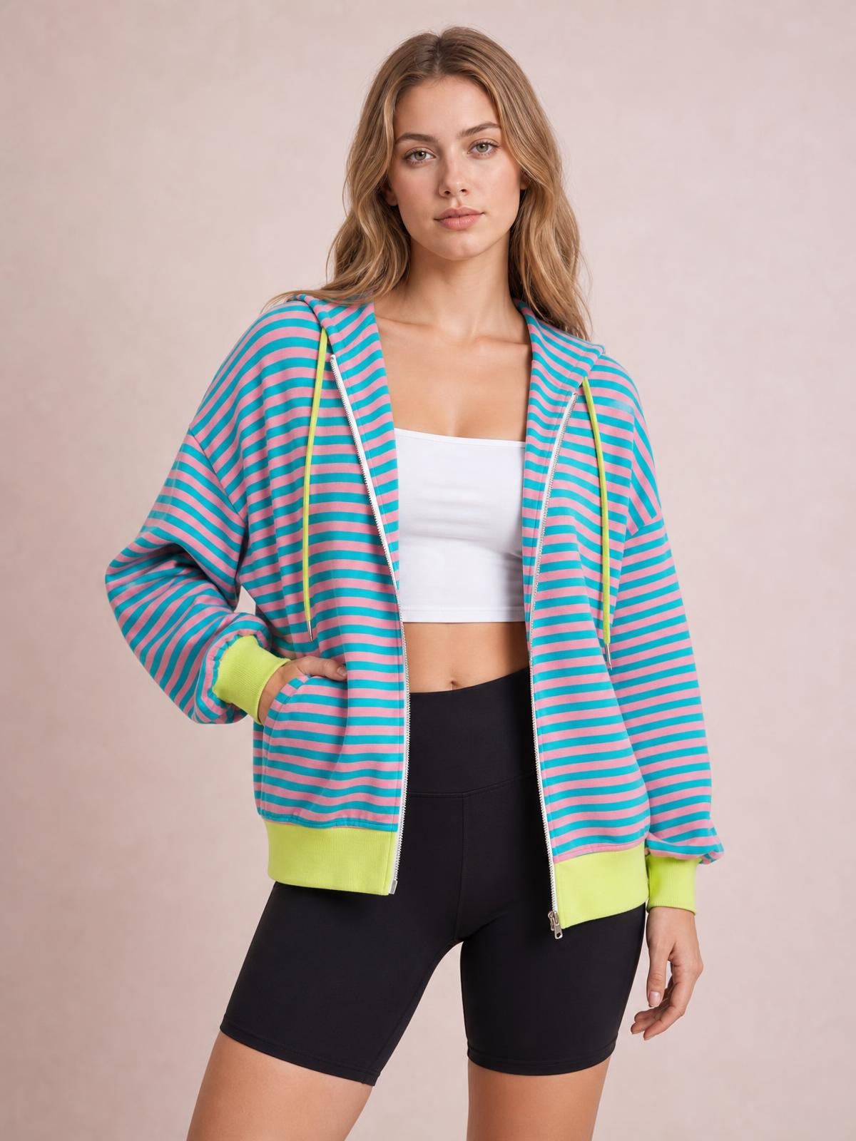 Model poses with one hand in the pocket wearing a turquoise and pink striped zip-up hoodie with a drawstring hood, long sleeves, and lime ribbed cuffs and hem.