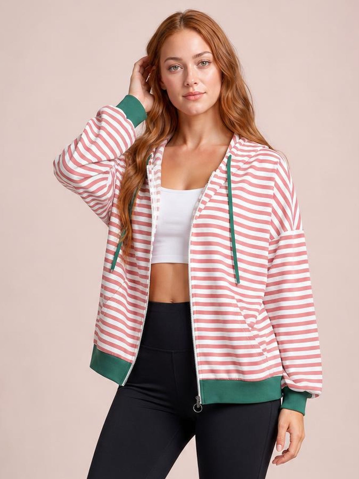 Model poses in a pink-and-white striped zip-up hoodie with long sleeves, green drawstrings and trim, ribbed cuffs, and a relaxed silhouette.