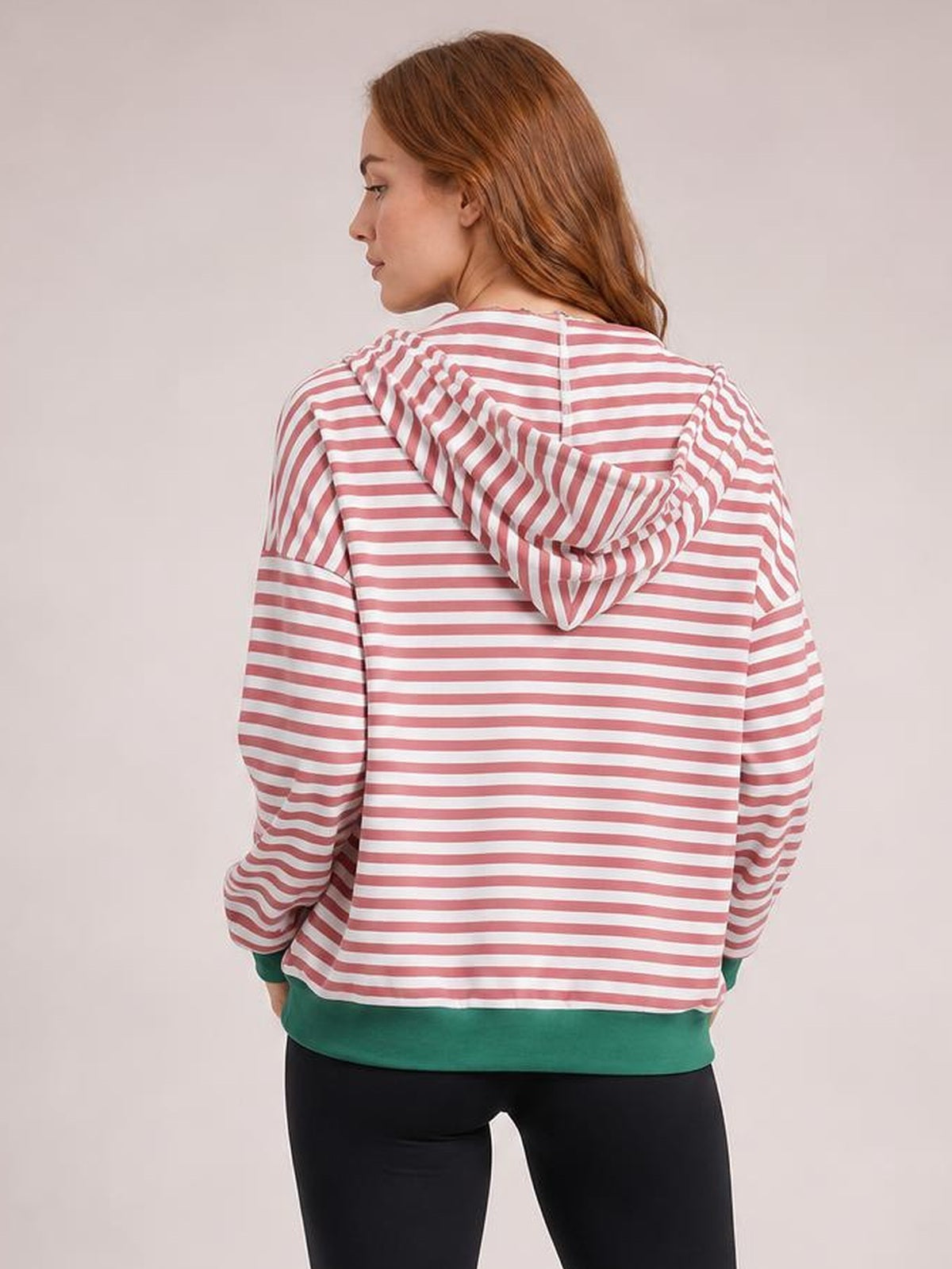 A model looks over her shoulder in a relaxed pink-and-white striped zip-up hoodie with a draped hood and long sleeves.