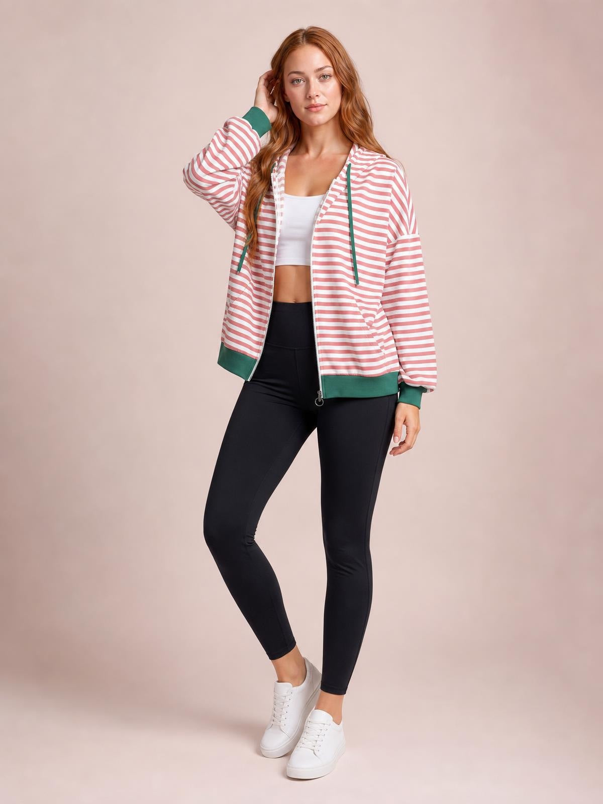A model poses in a pink-and-white striped zip-up long-sleeve hoodie with green trim, drawstrings, pockets, and a relaxed silhouette.