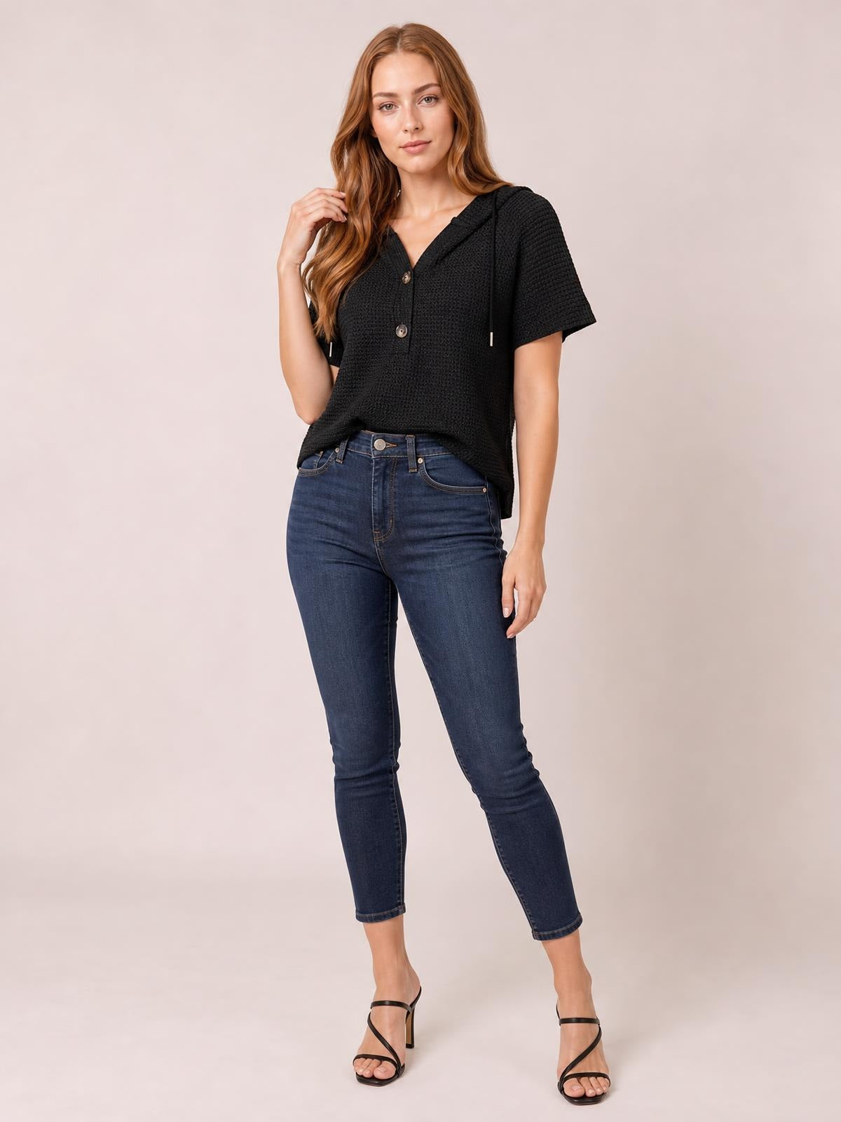 A model poses in a black waffle-knit short-sleeve hooded top with drawstrings, button front, and a relaxed silhouette.