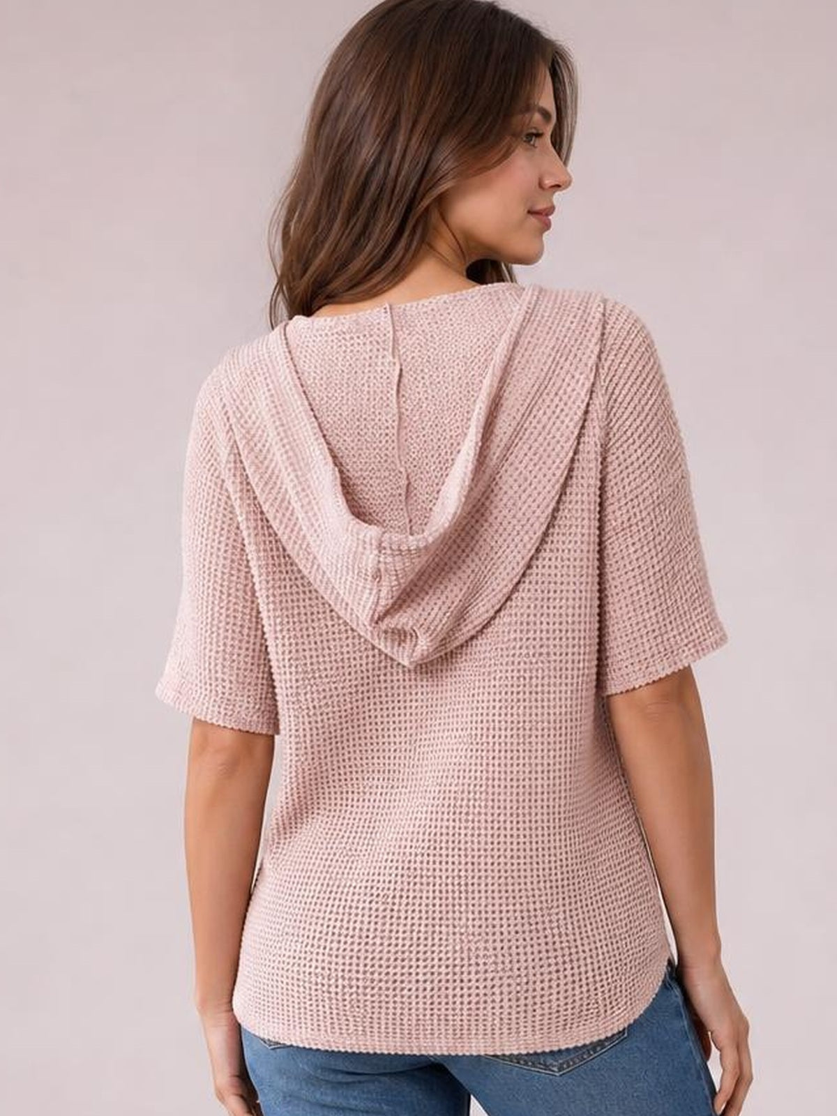 A model wears a soft pink waffle-knit short sleeve hooded top with a relaxed, straight silhouette and draped hood, shown from the back.
