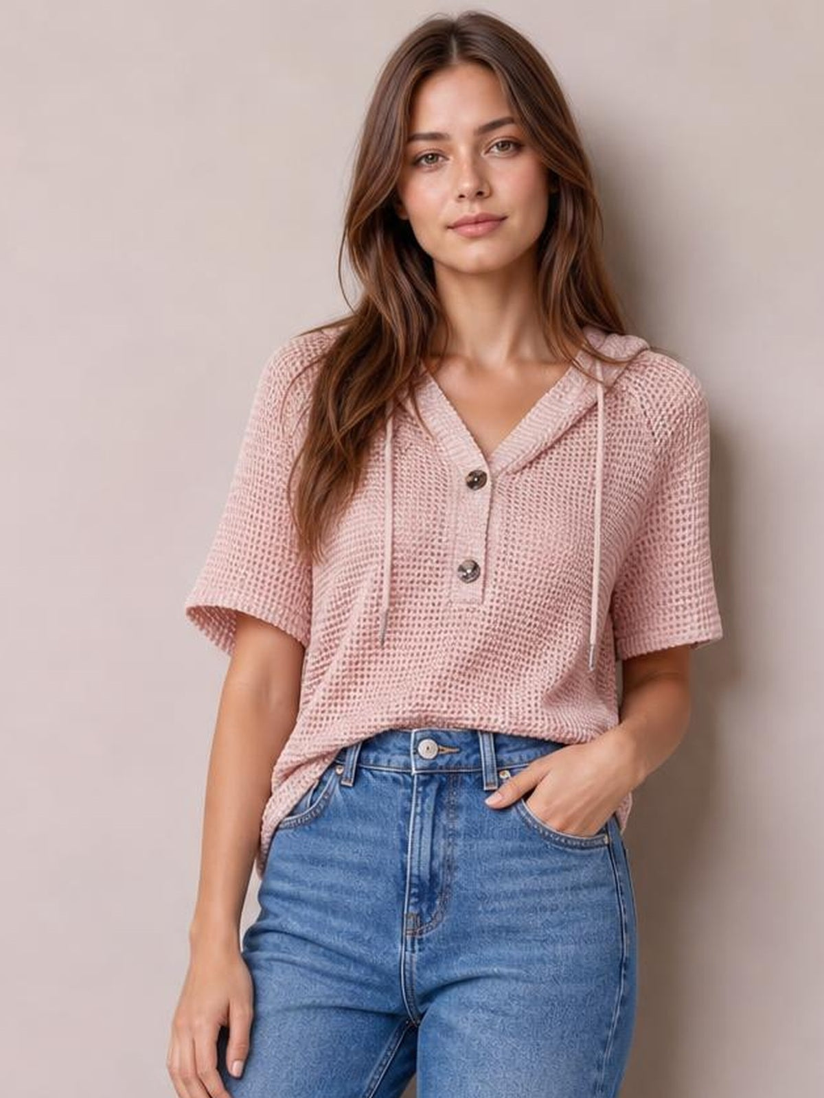 Model poses in a pink waffle-knit short-sleeve hooded top with drawstrings, a buttoned V-neck placket, and relaxed cropped silhouette.