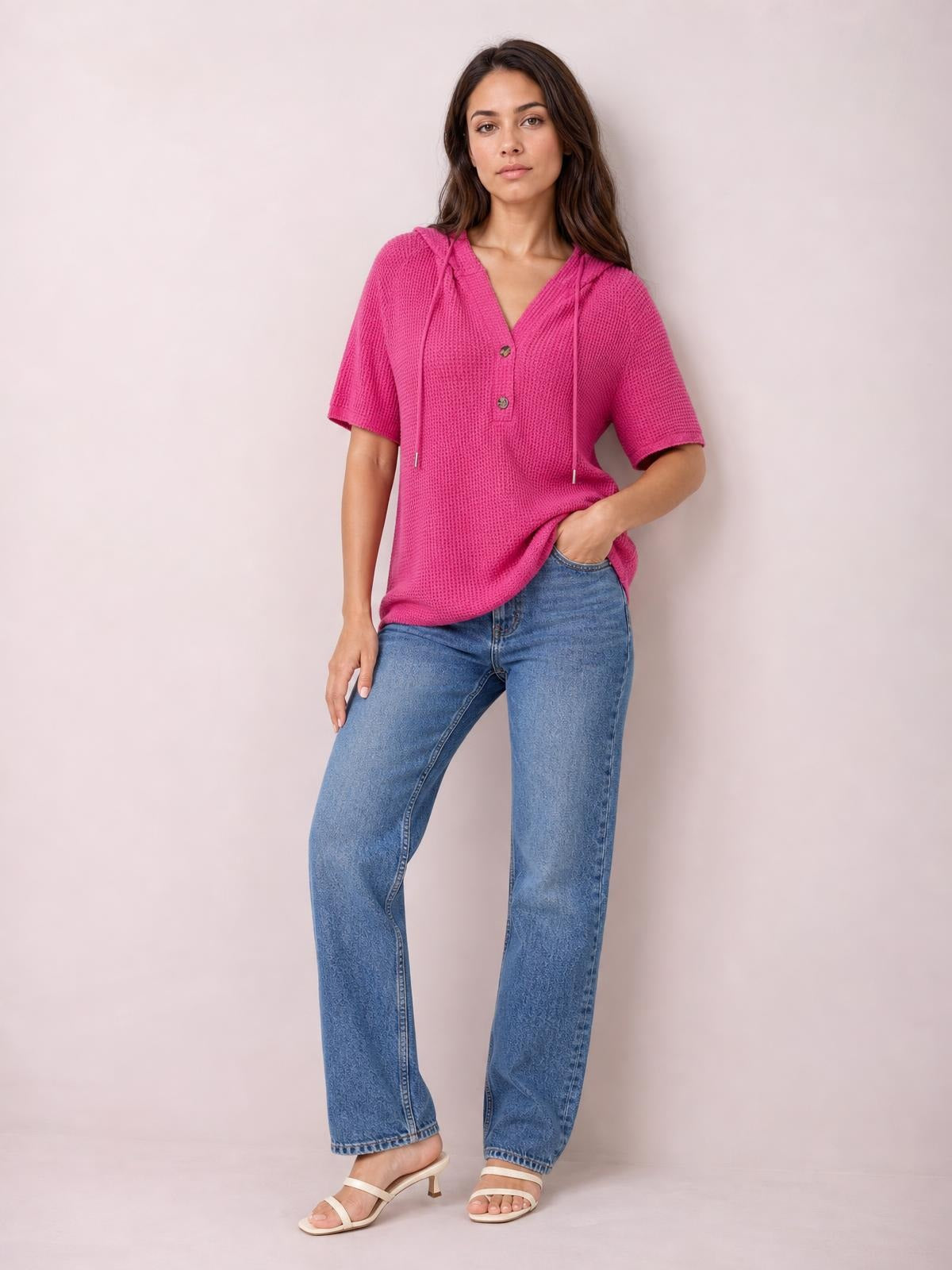 Model wears a bright pink waffle-knit short-sleeve hooded top with drawstrings and button placket, shown in a relaxed fit with one hand in a pocket.