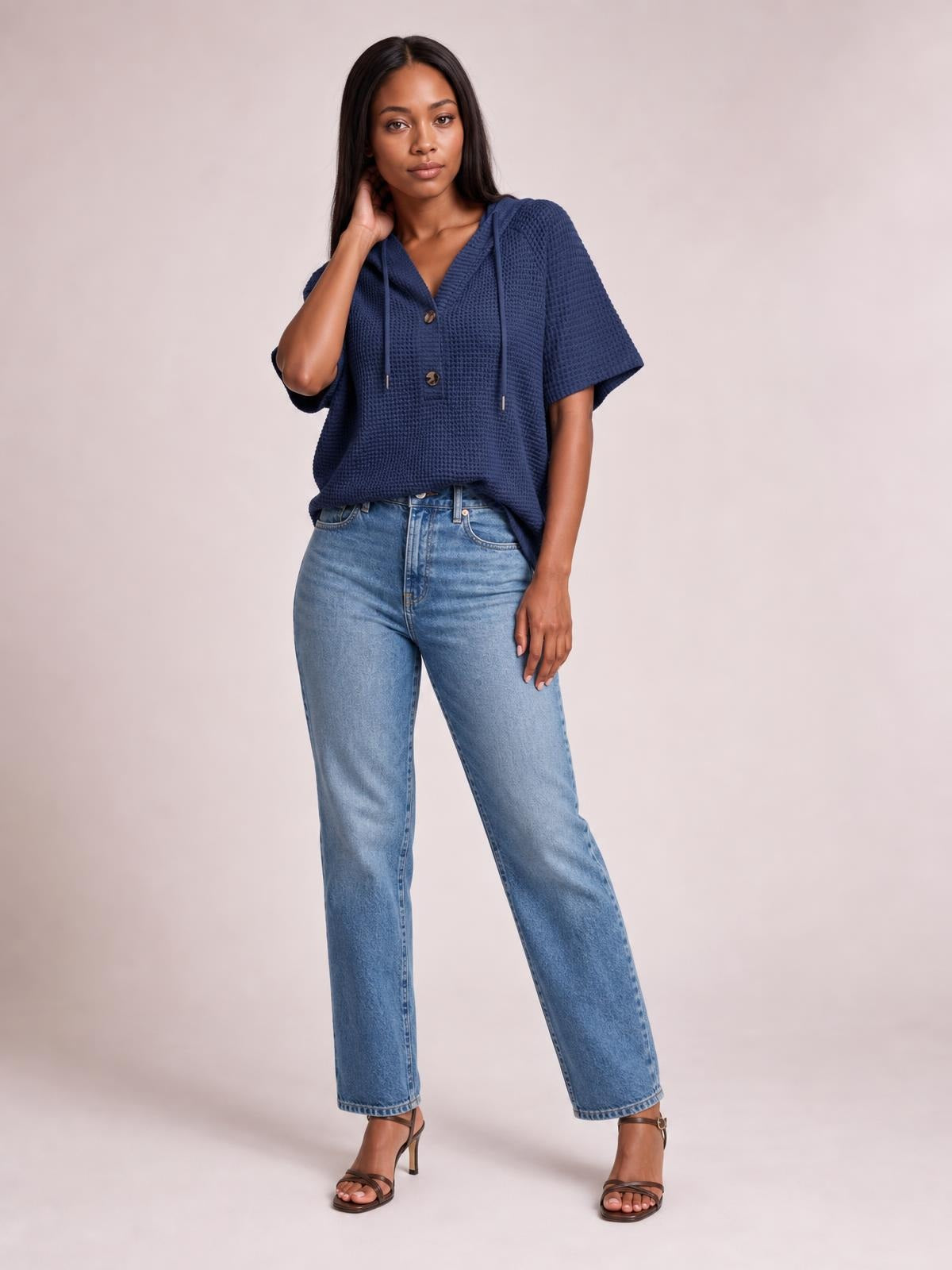 Model poses in a navy waffle-knit hooded top with short sleeves, drawstrings, button front, and a relaxed, boxy silhouette.
