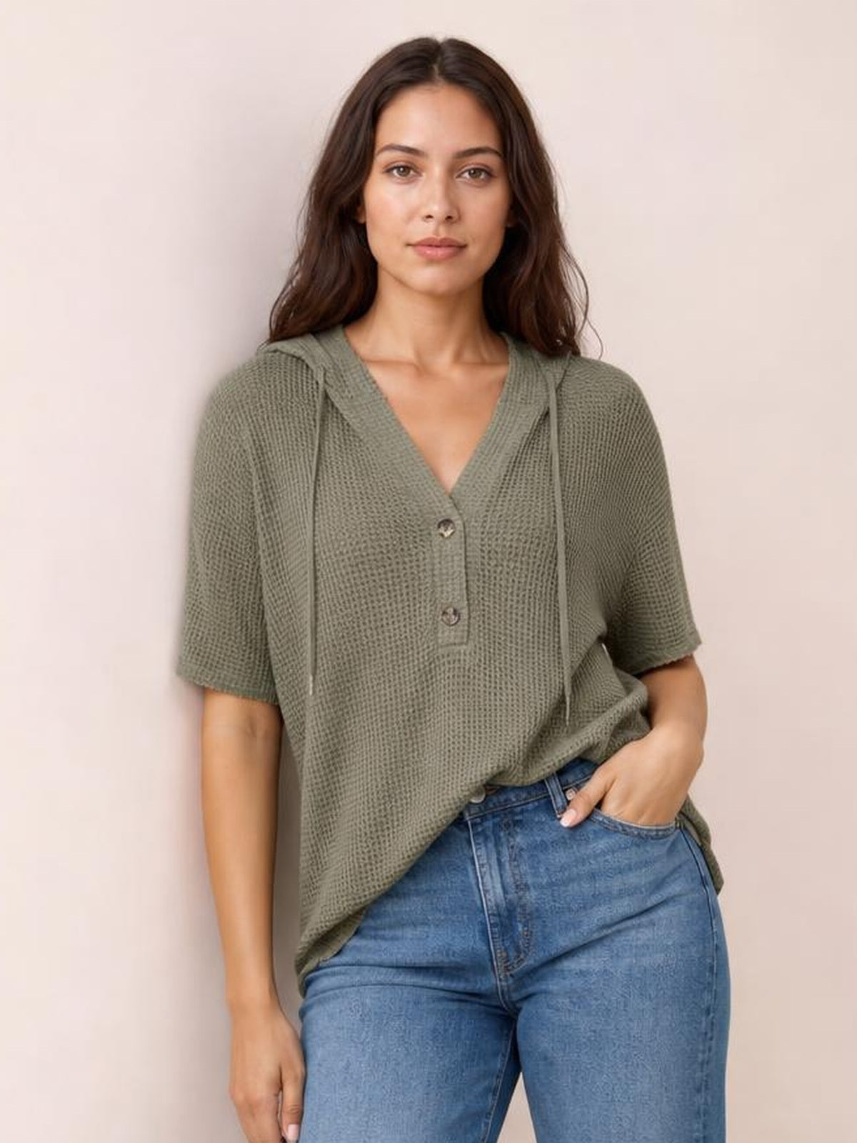 A model wears an olive green waffle-knit hooded top with short sleeves, drawstring details, a buttoned V-neck placket, and a relaxed silhouette.