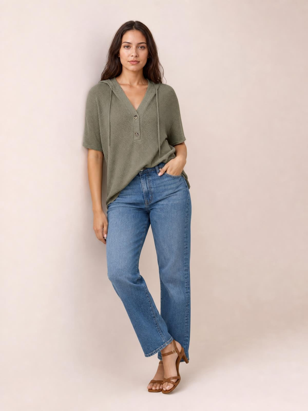 A woman poses in an olive-green waffle-knit short-sleeve hooded top with drawstrings, buttoned V-neck, and relaxed silhouette, paired with jeans.