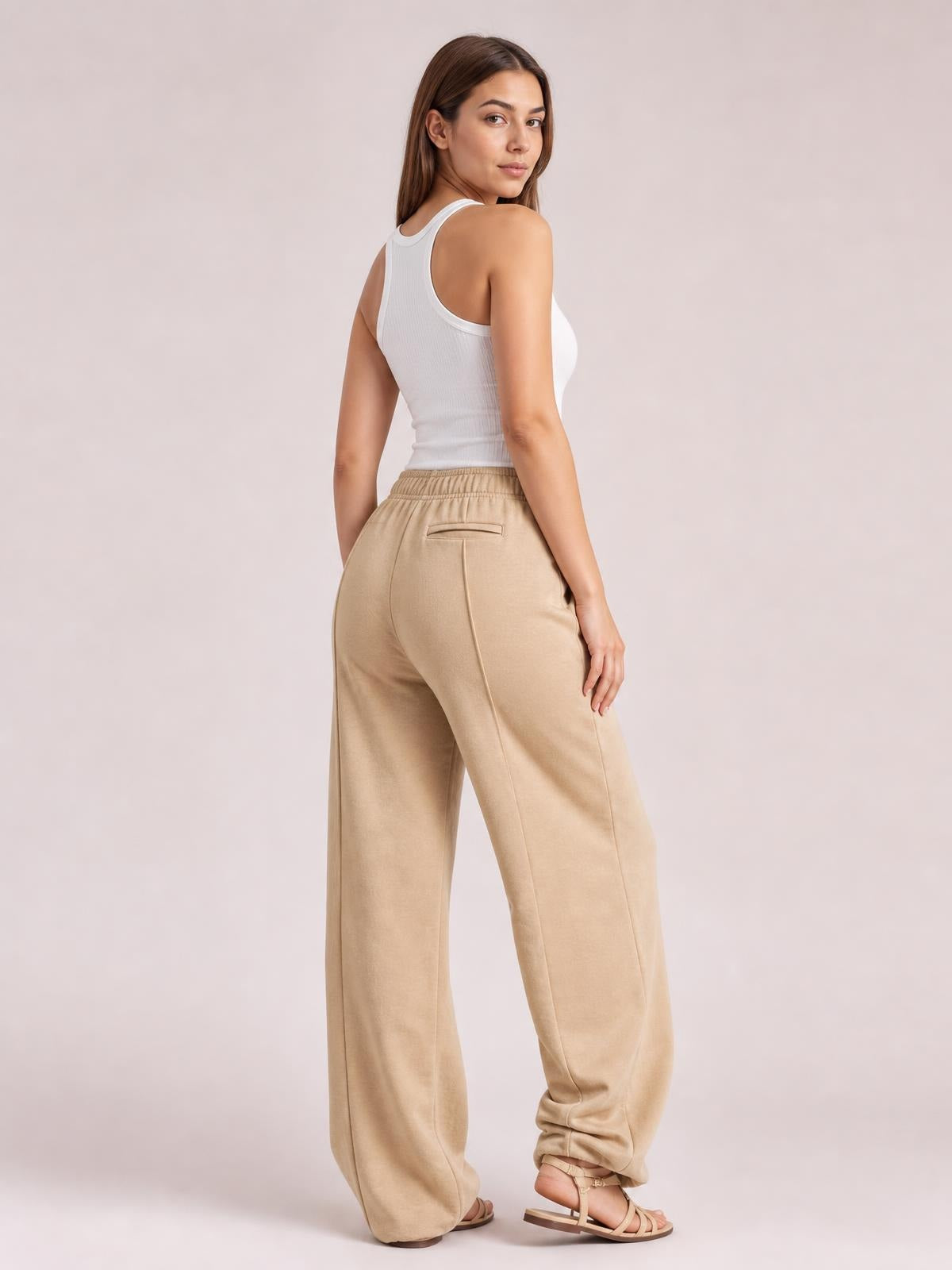Model turns to show beige drawstring wide leg pants with an elastic waist, pocketed construction, and relaxed full-length silhouette.
