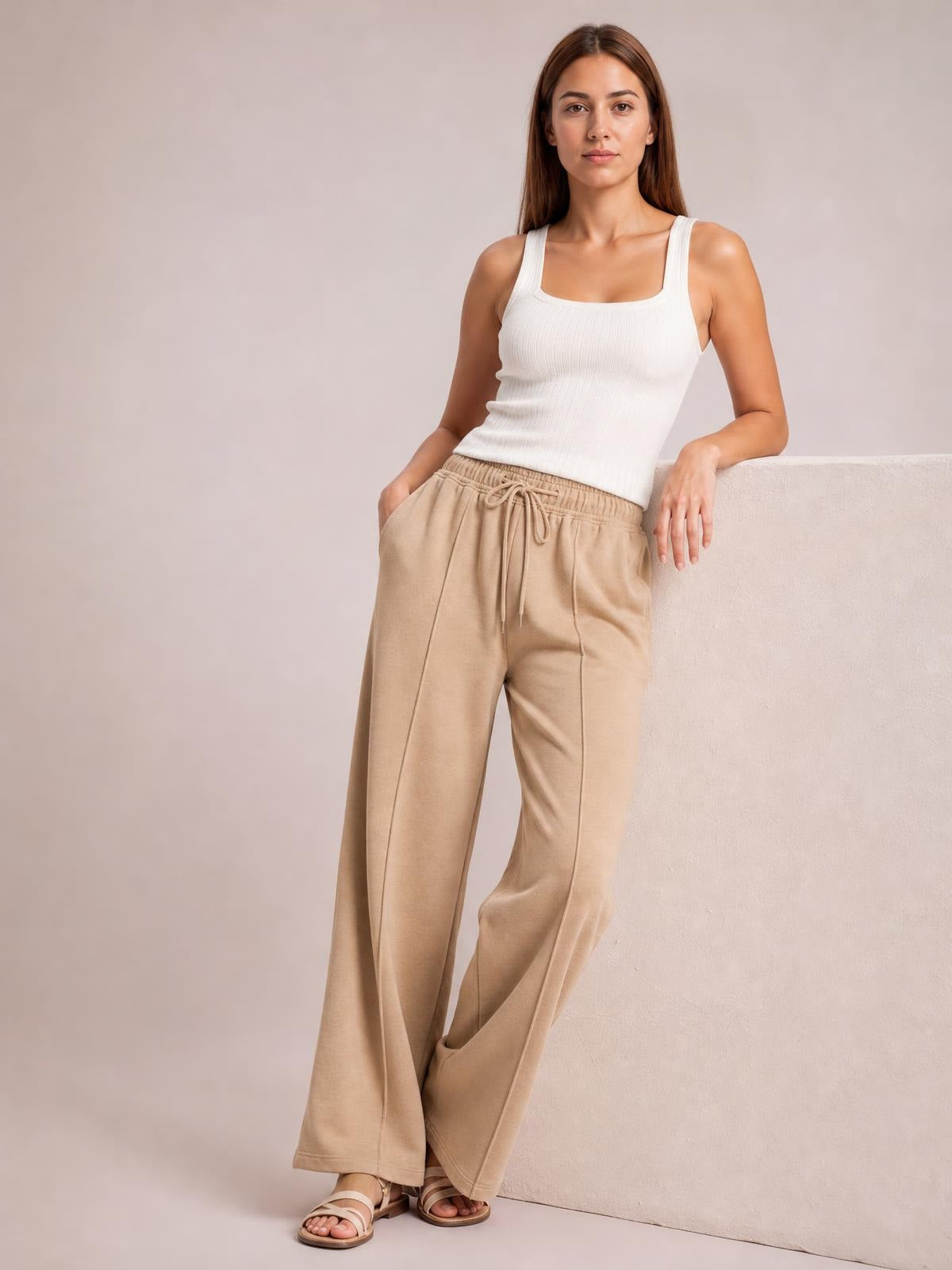 Model wears beige drawstring wide-leg pants with visible pockets and an elastic waist, posing with one hand in a pocket.