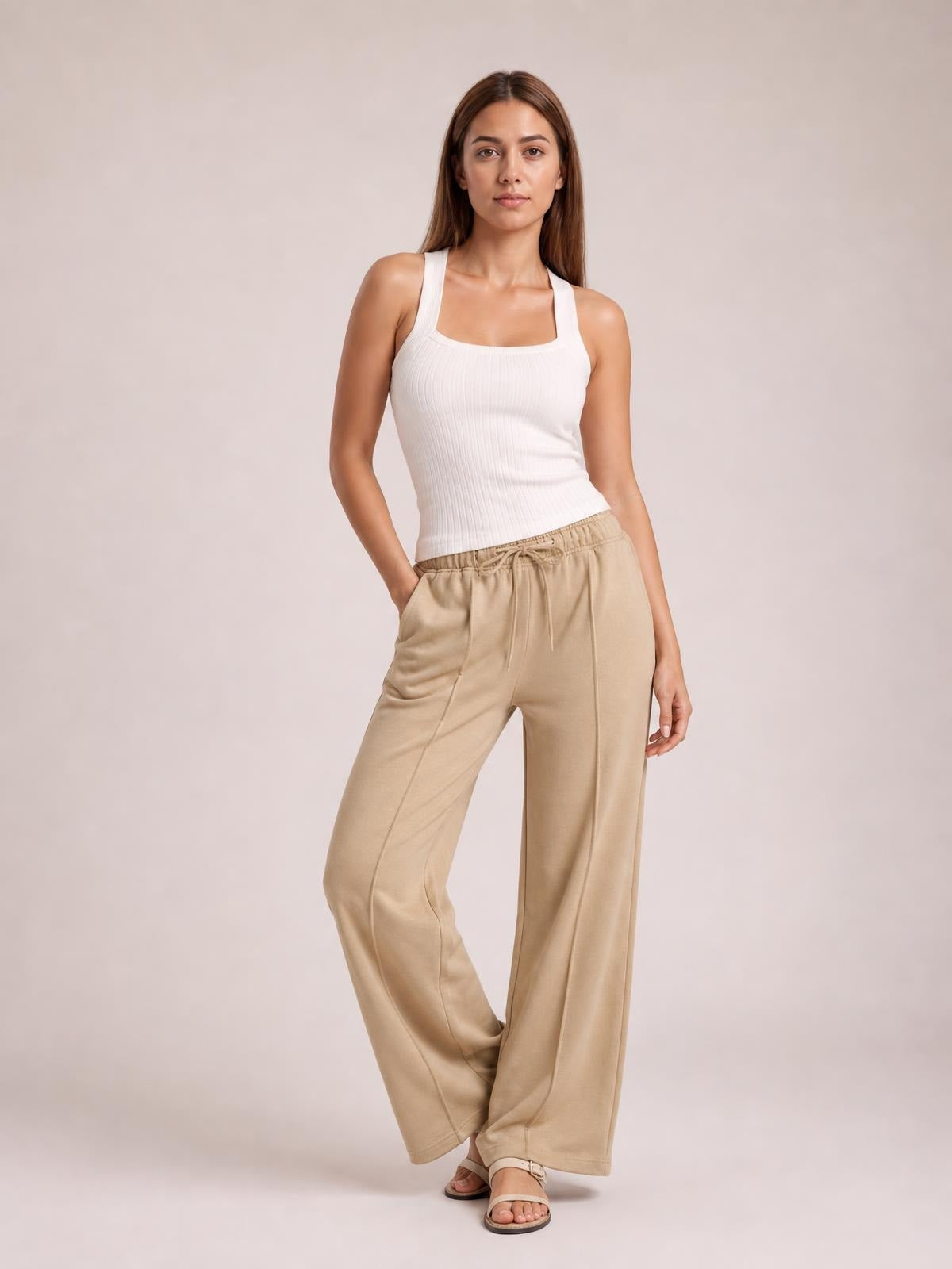 Model poses in beige drawstring wide leg pants with pockets, featuring a relaxed silhouette, elasticized waist, and straight construction.