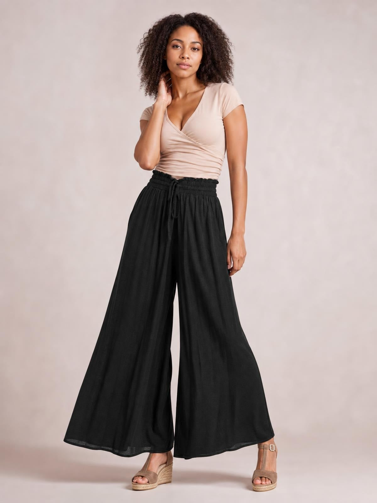 Model poses in black drawstring wide leg pants with a gathered elastic waist, flowing oversized silhouette, and full-length hems.