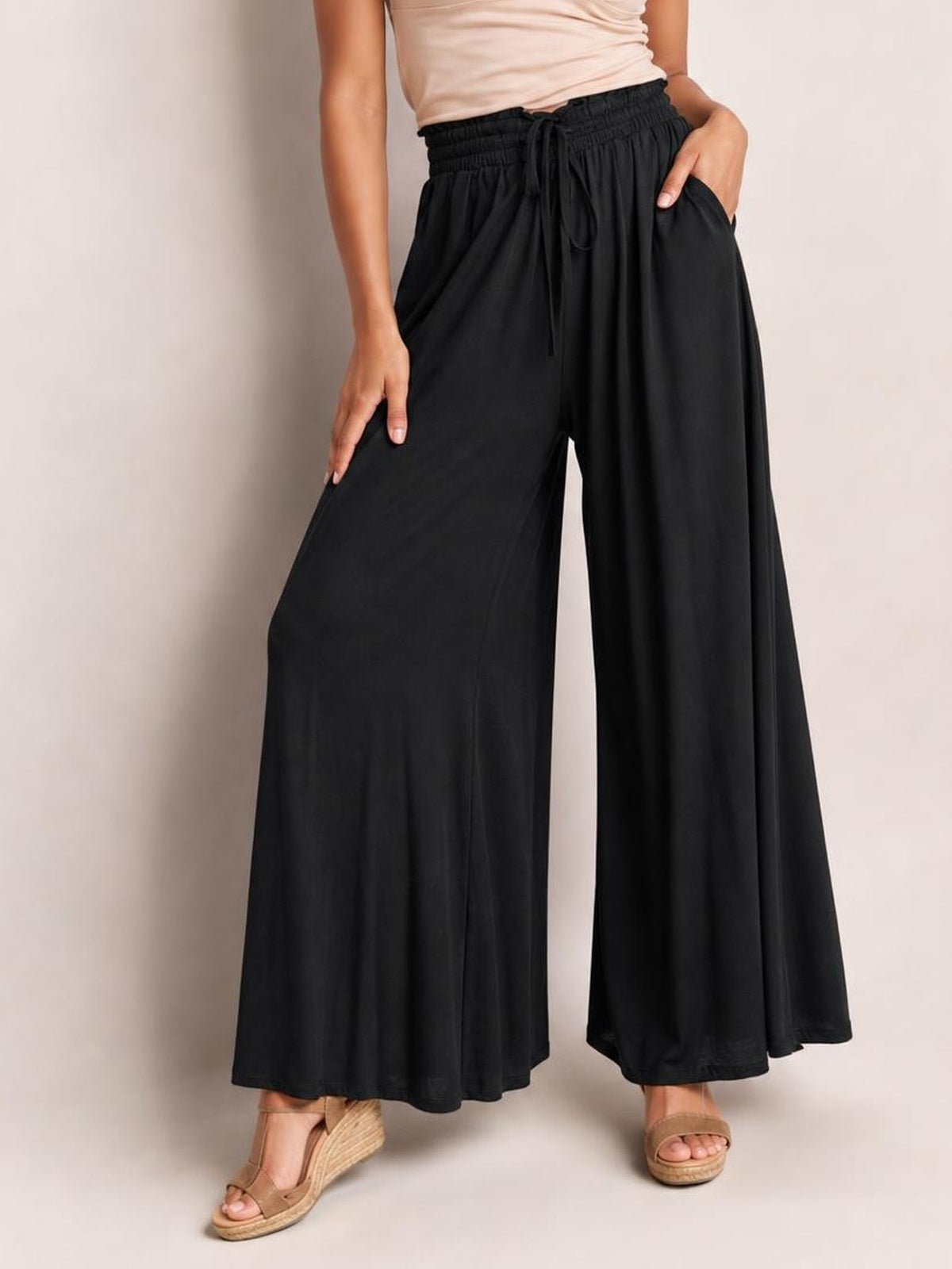 Model poses in black drawstring wide leg pants with an elastic waist, flowing silhouette, and visible side pockets.