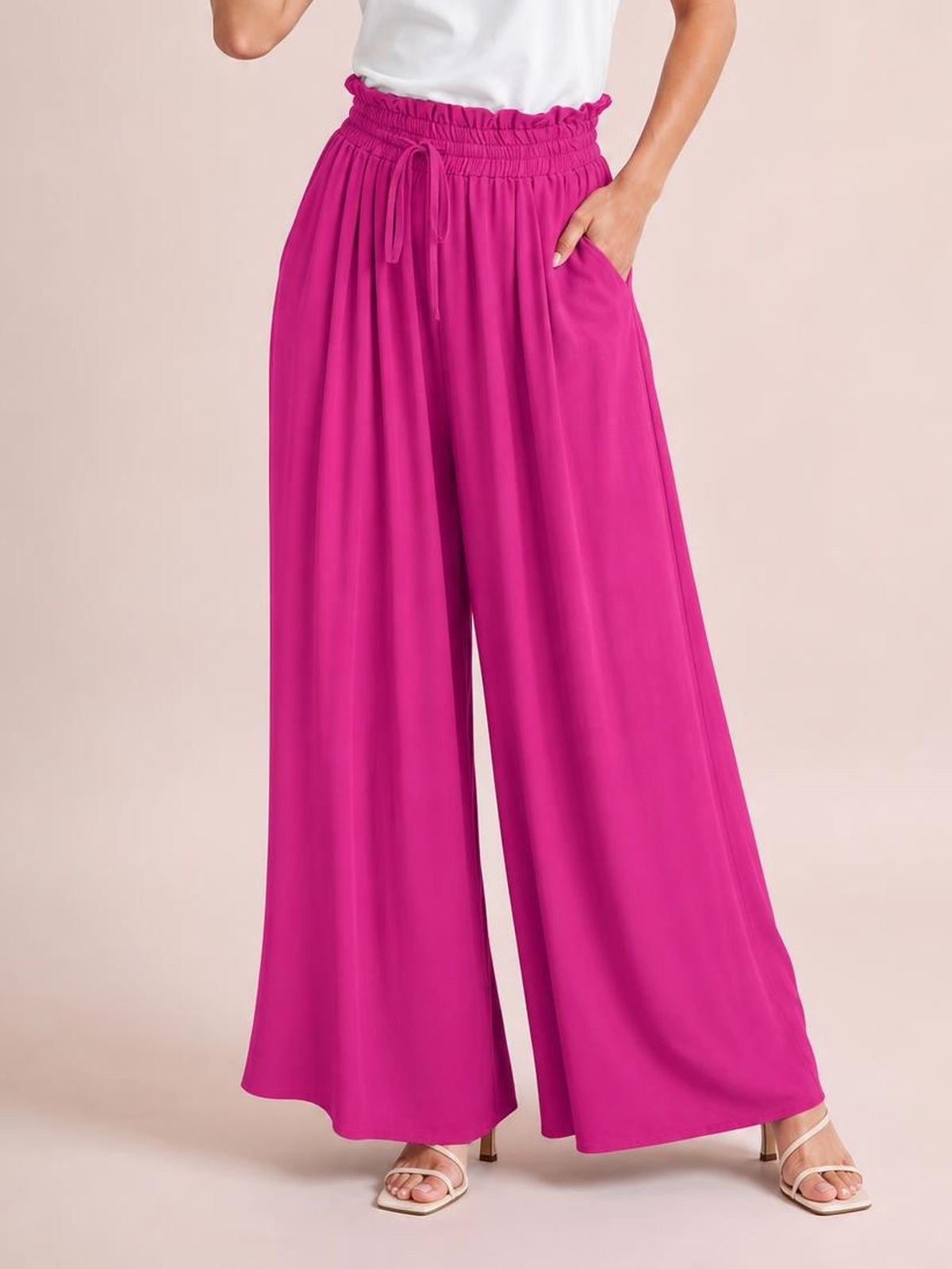 Model wearing fuchsia drawstring wide-leg pants with an elastic waistband, flowing silhouette, and side pockets, posing with one hand tucked into a pocket.