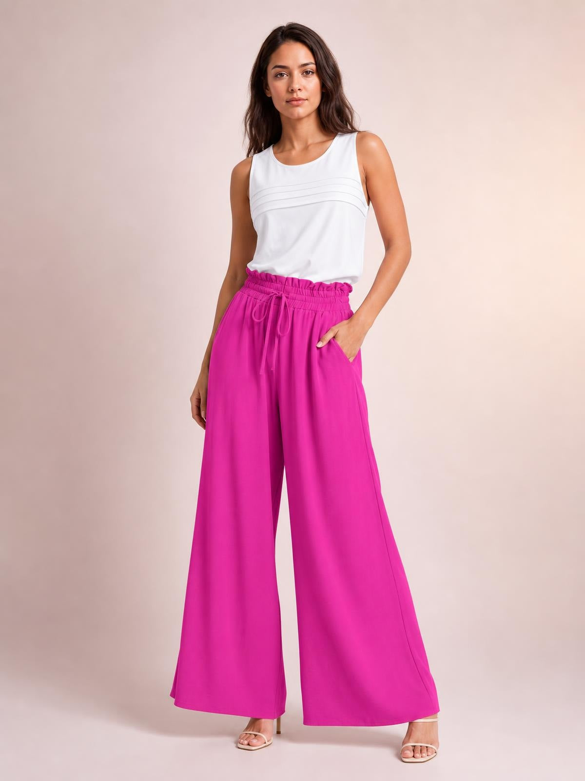 Model poses in bright pink drawstring wide leg pants with a relaxed flowy silhouette, elastic waistband, and visible side pockets.